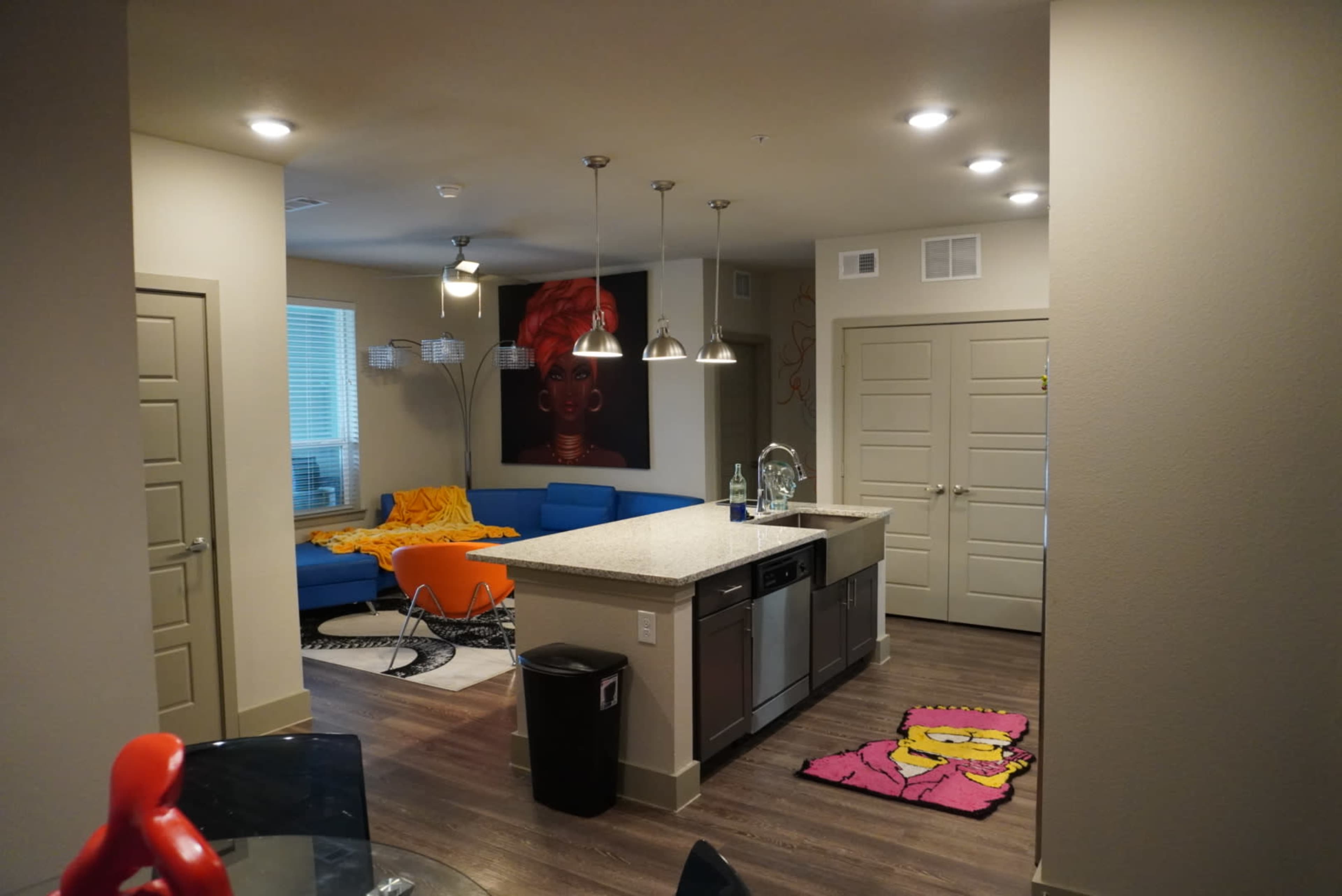 A modern living space with an open kitchen featuring stainless steel appliances, a blue couch, and colorful decor.