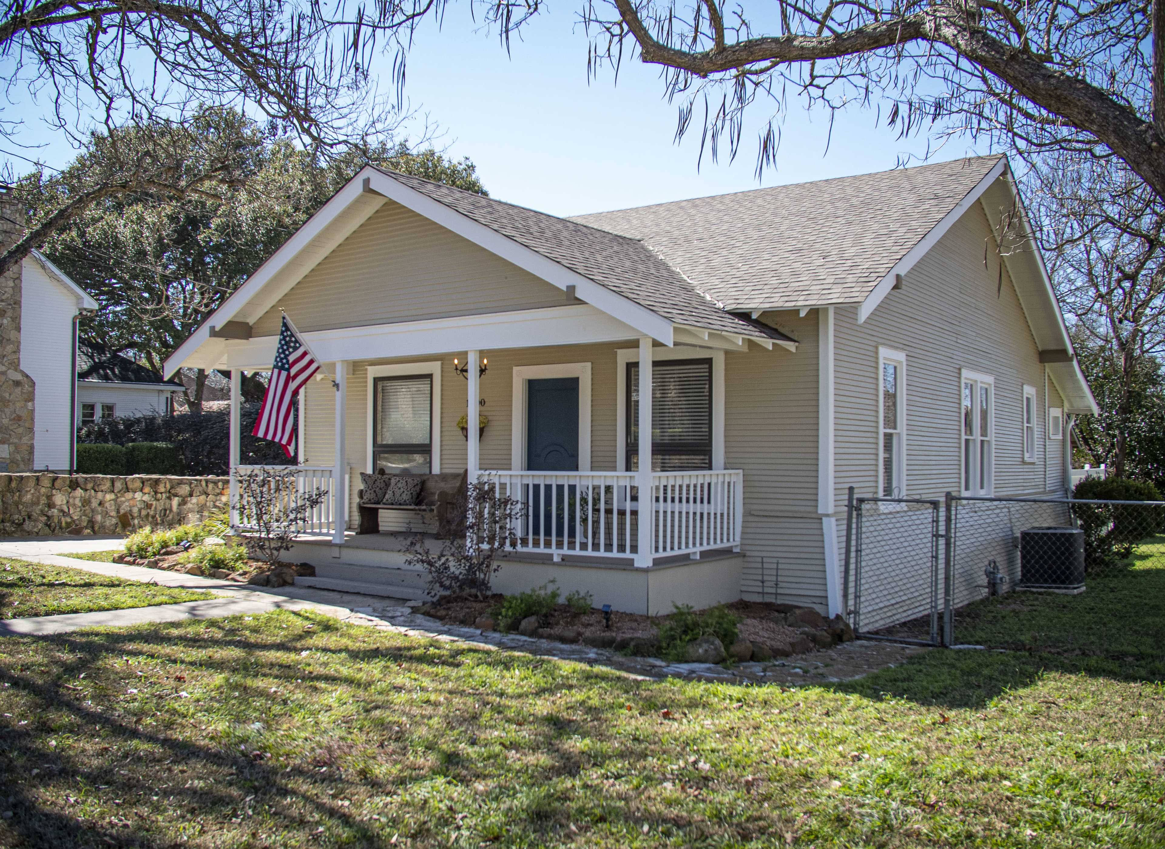 A single-story house with a front porch, an American flag hanging, and a well-maintained yard.