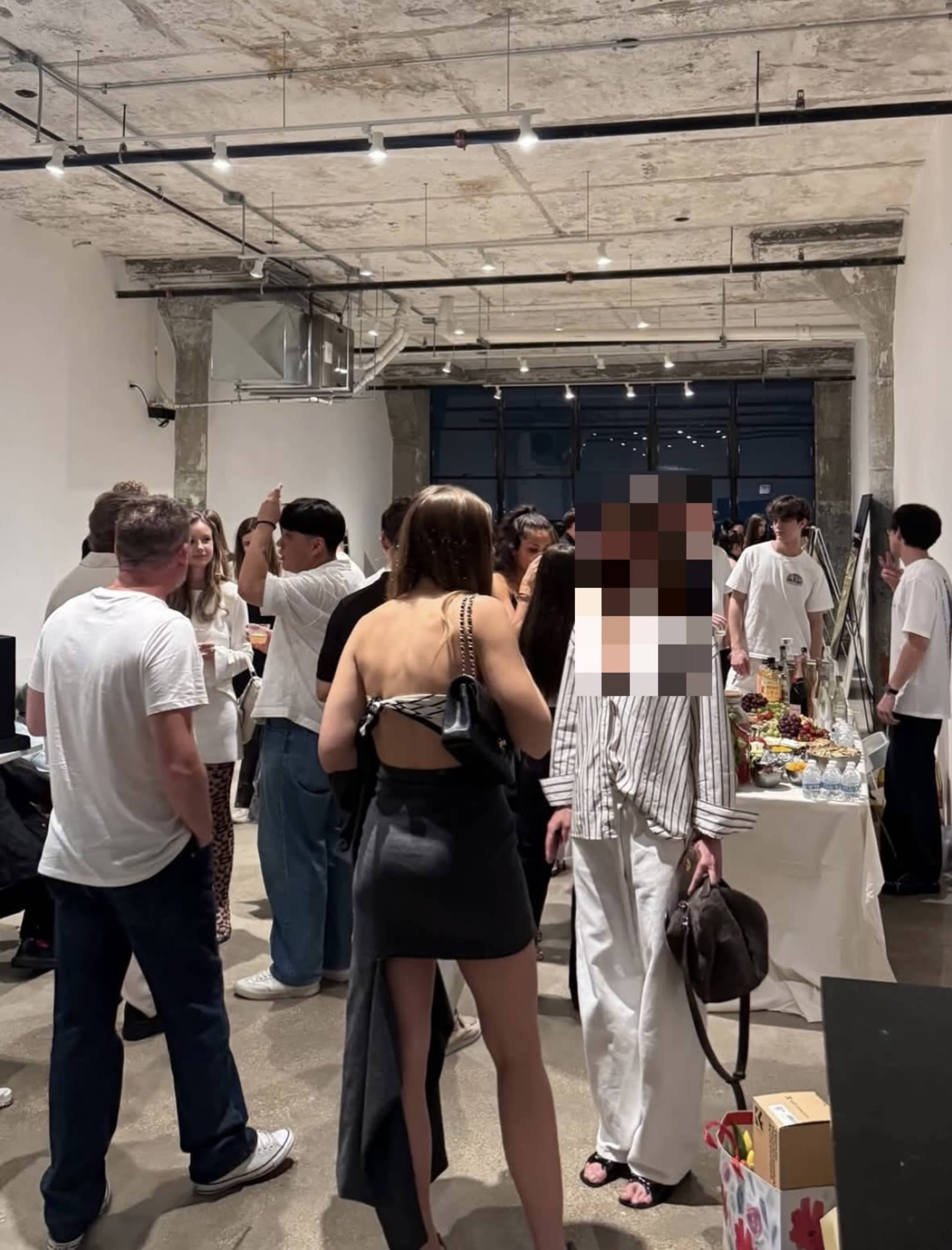 A crowd of people mingles in a spacious gallery-like setting with concrete walls and overhead lights.