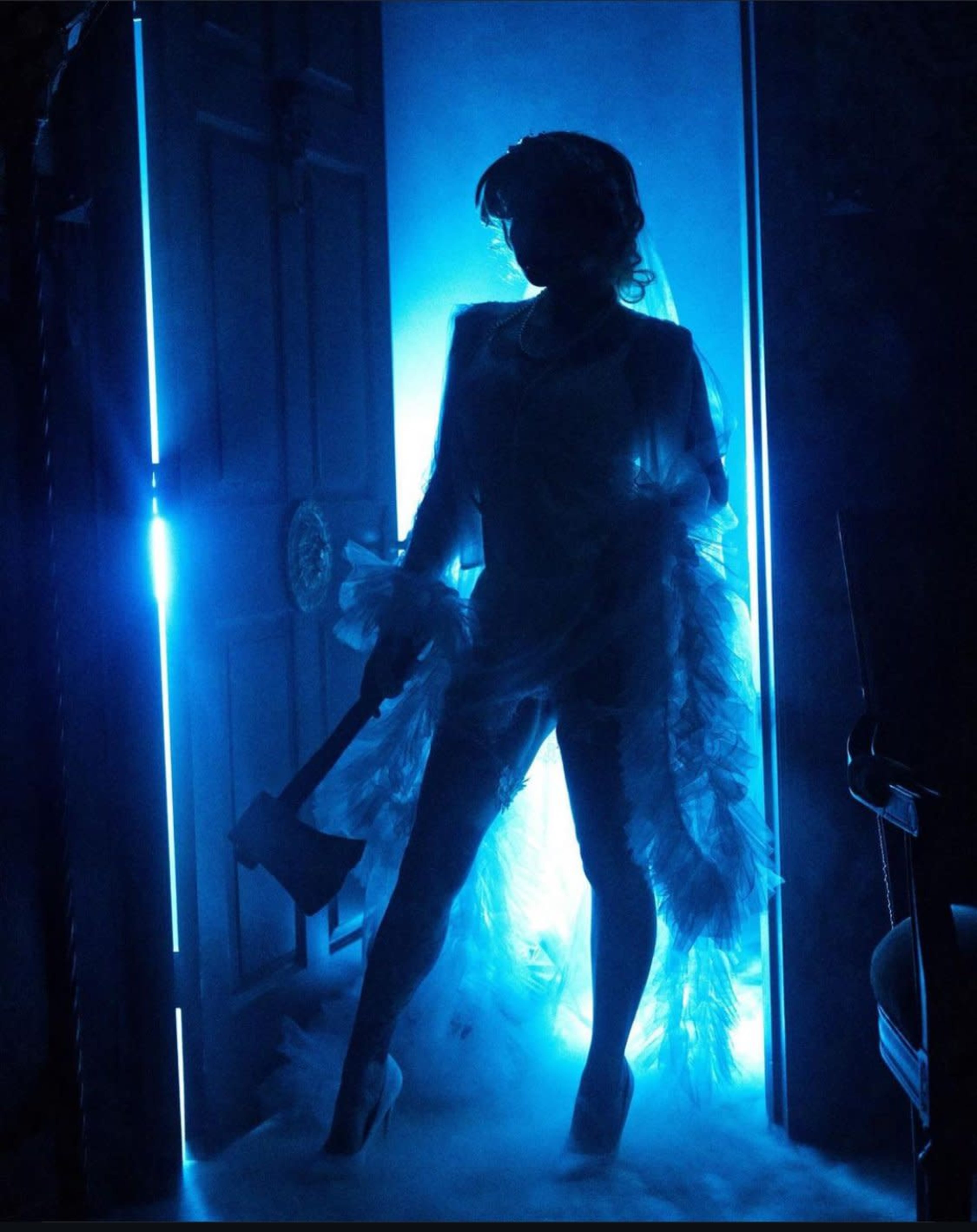 A figure stands in a doorway illuminated by blue light, holding an axe and partially shrouded in mist.