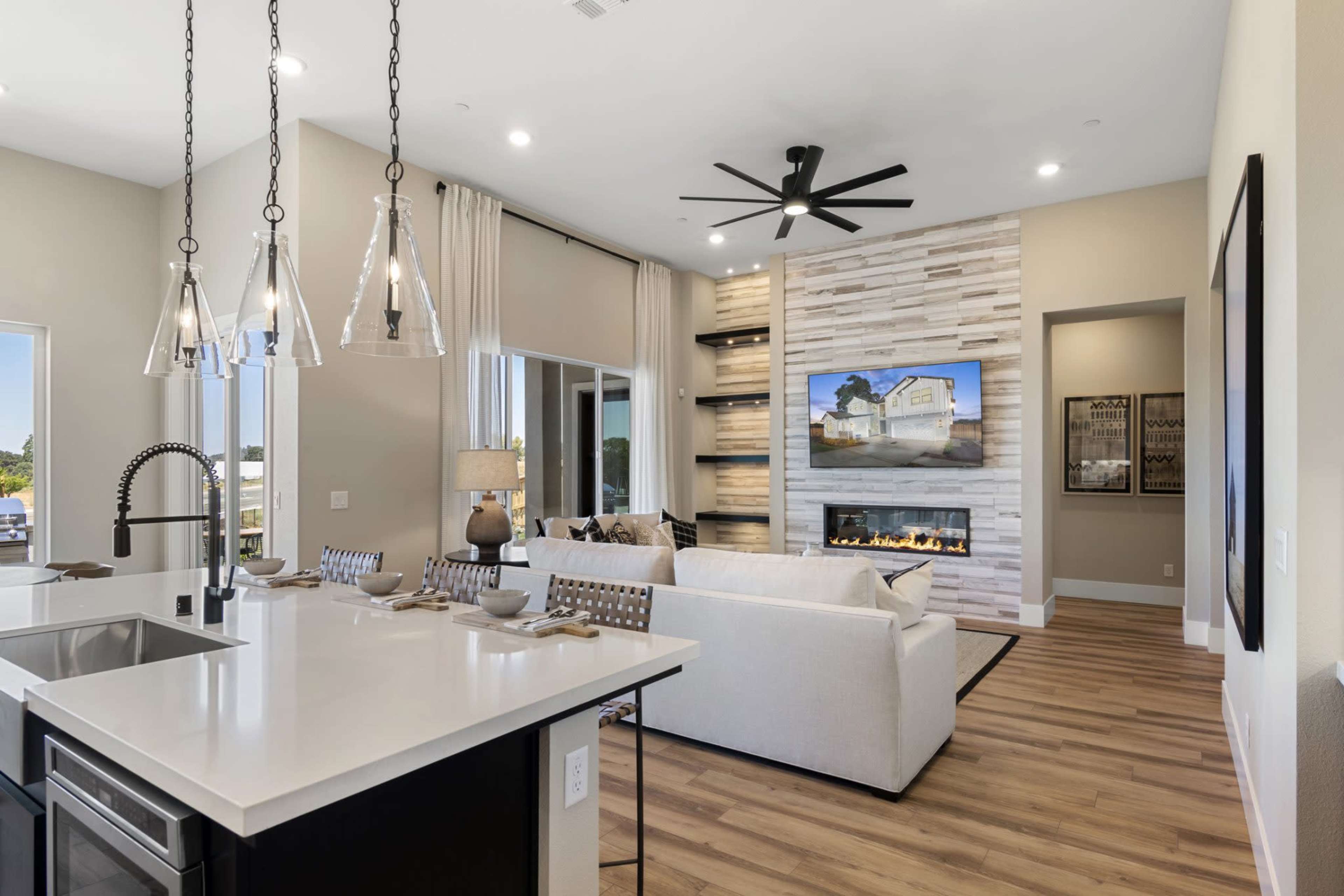 The image shows a modern living room with a white sofa, dark cabinets, a fireplace, and a large television mounted on a stone wall.