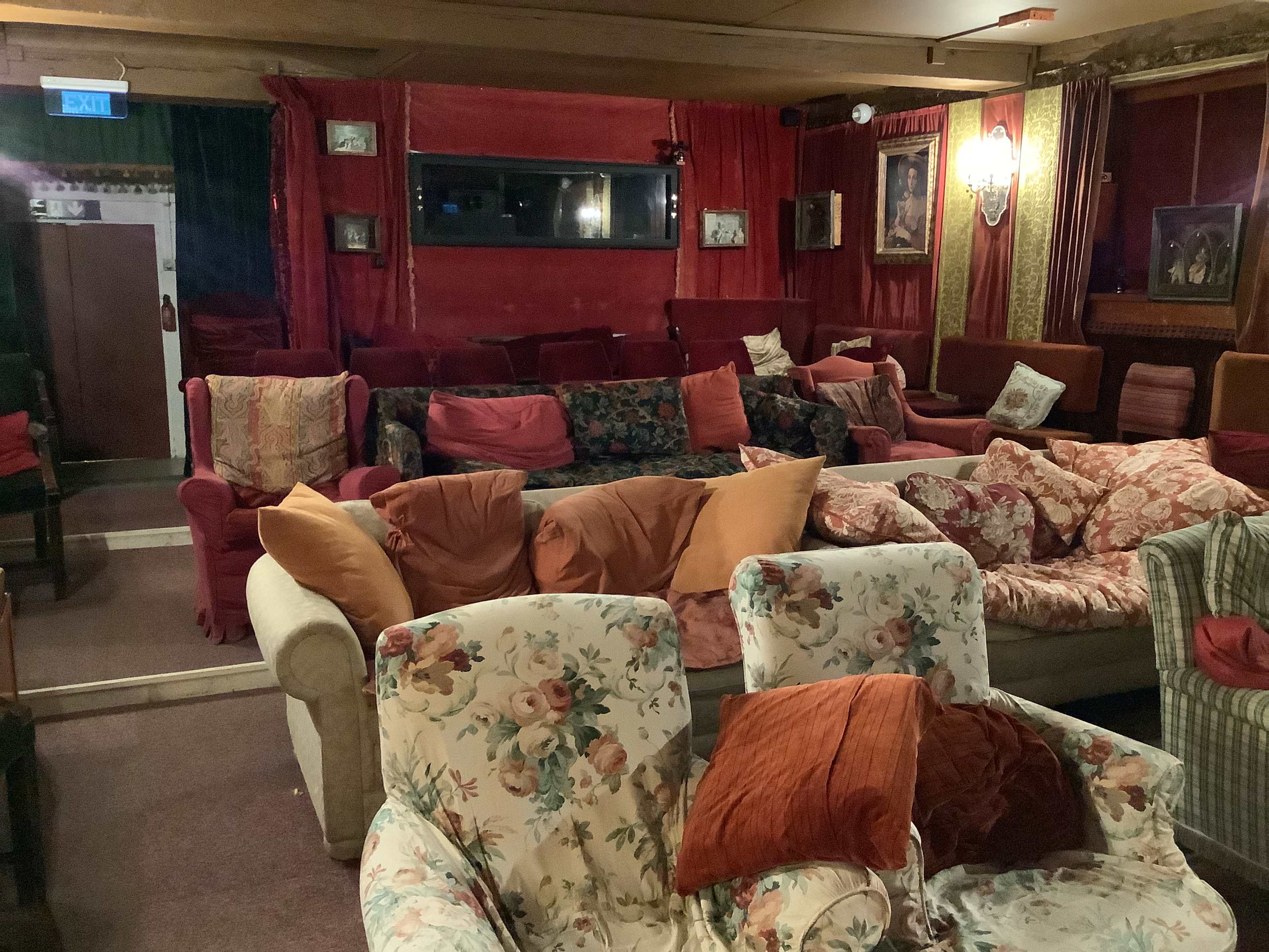 A cozy lounge area filled with a variety of colorful sofas and armchairs arranged around a dimly lit space.