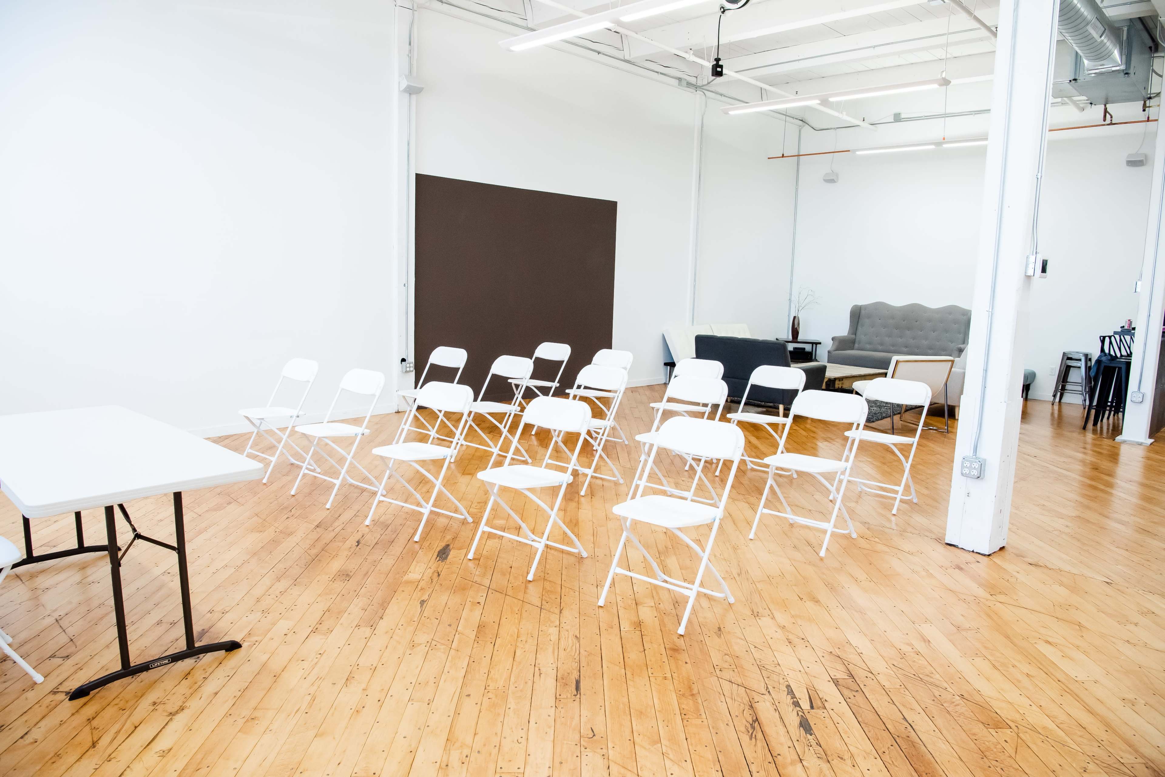 A spacious indoors area with white folding chairs arranged in rows facing a gray couch and side table.