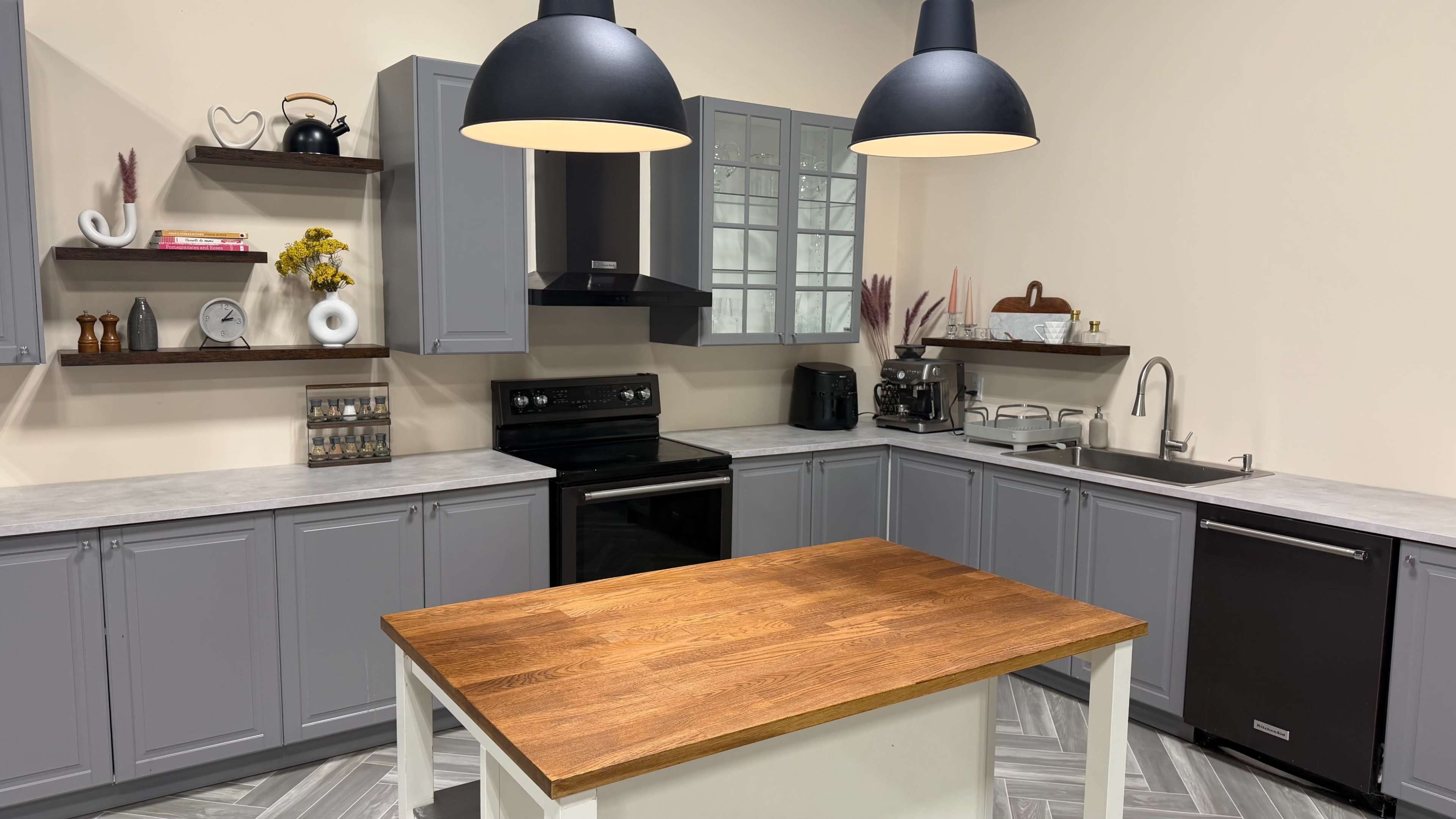 A modern kitchen features gray cabinets, a wooden island table, and pendant lighting, with appliances and decor arranged neatly.