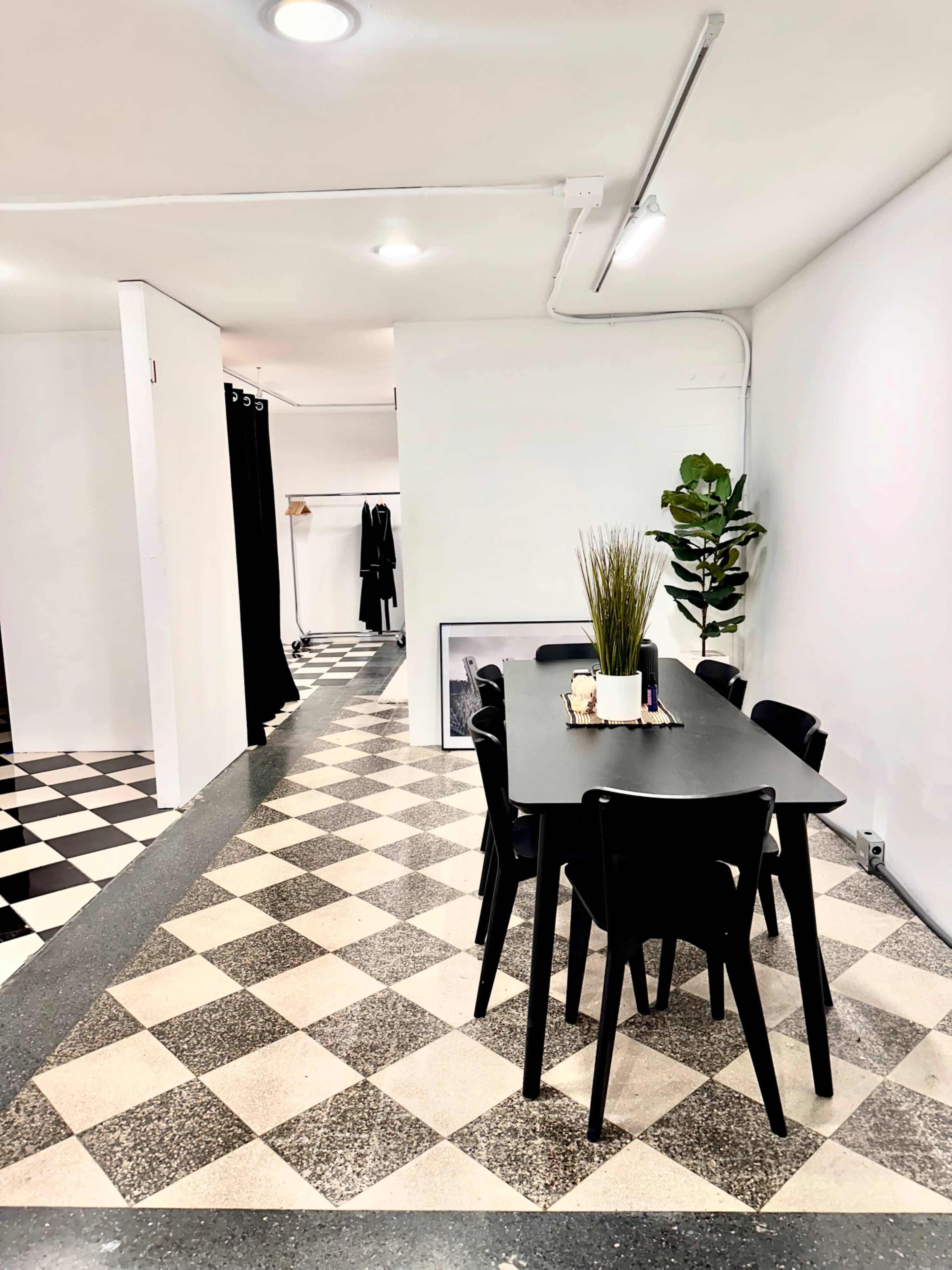 The image shows a modern dining area with a black table surrounded by six chairs, set against a backdrop of checkered flooring and clean white walls.