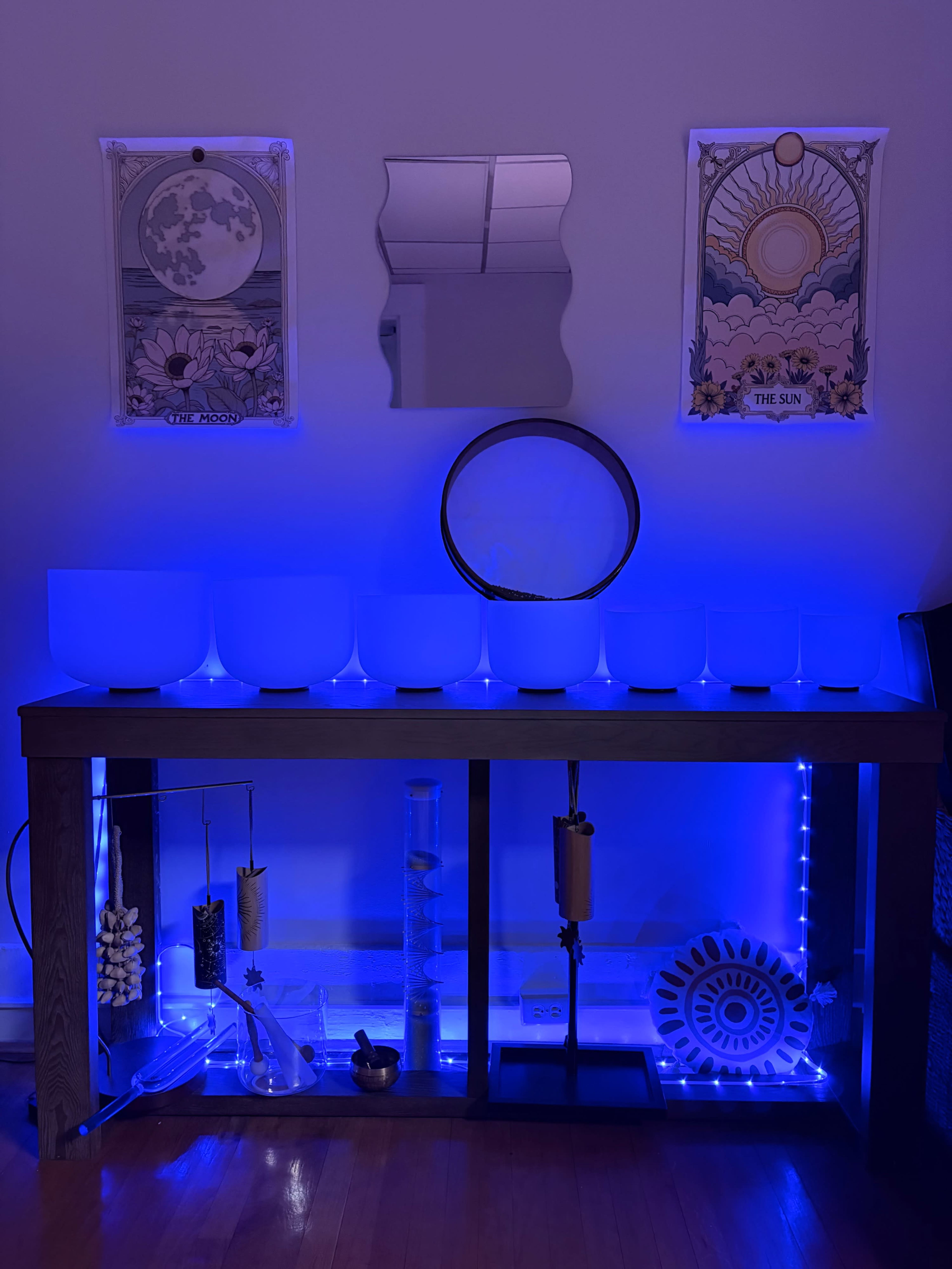A wooden table with blue LED lighting features several crystal bowls, decorative objects, and framed artwork above it.