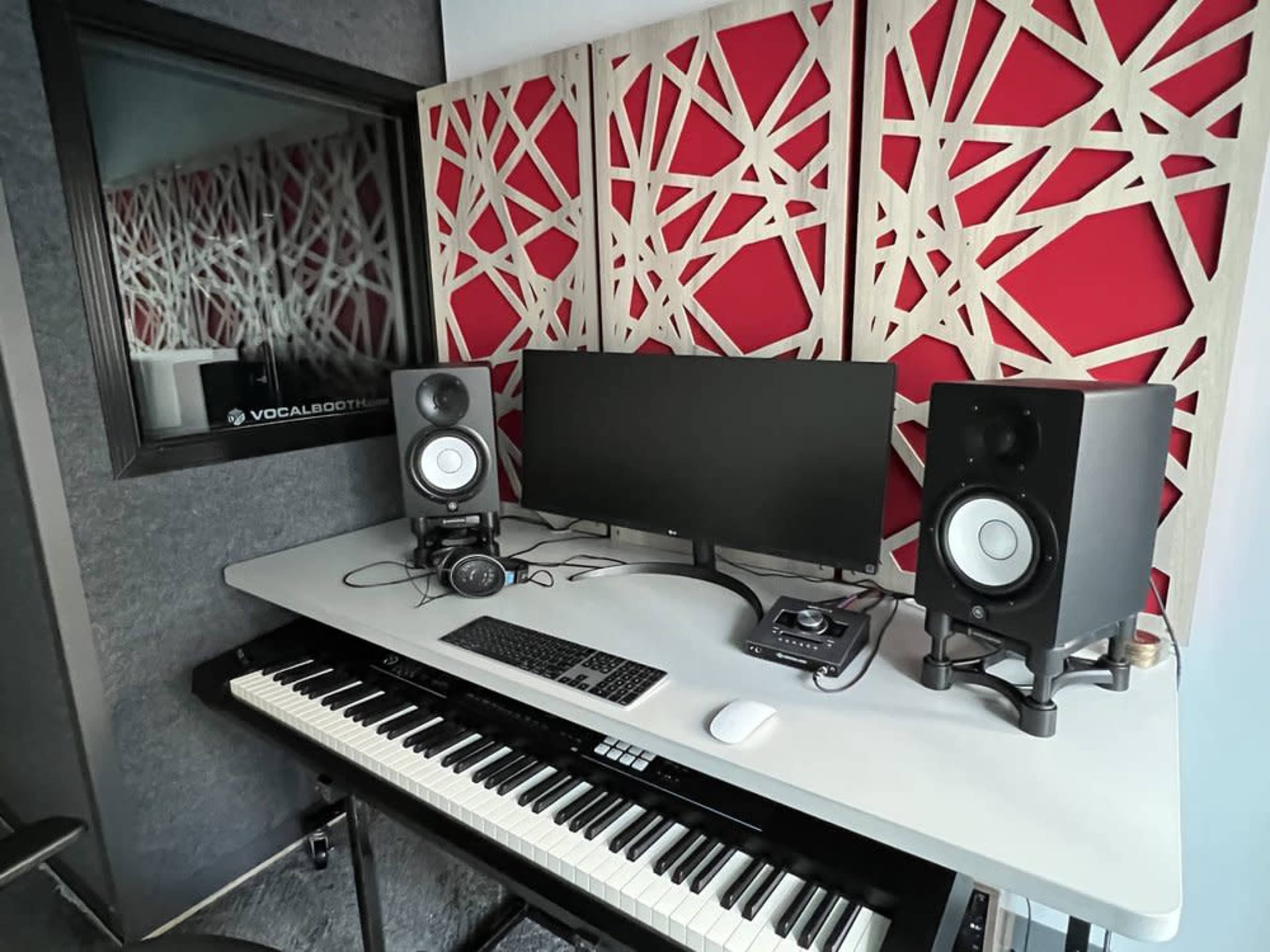 The image shows a modern recording studio featuring a keyboard, computer monitor, studio monitors, and soundproof walls.
