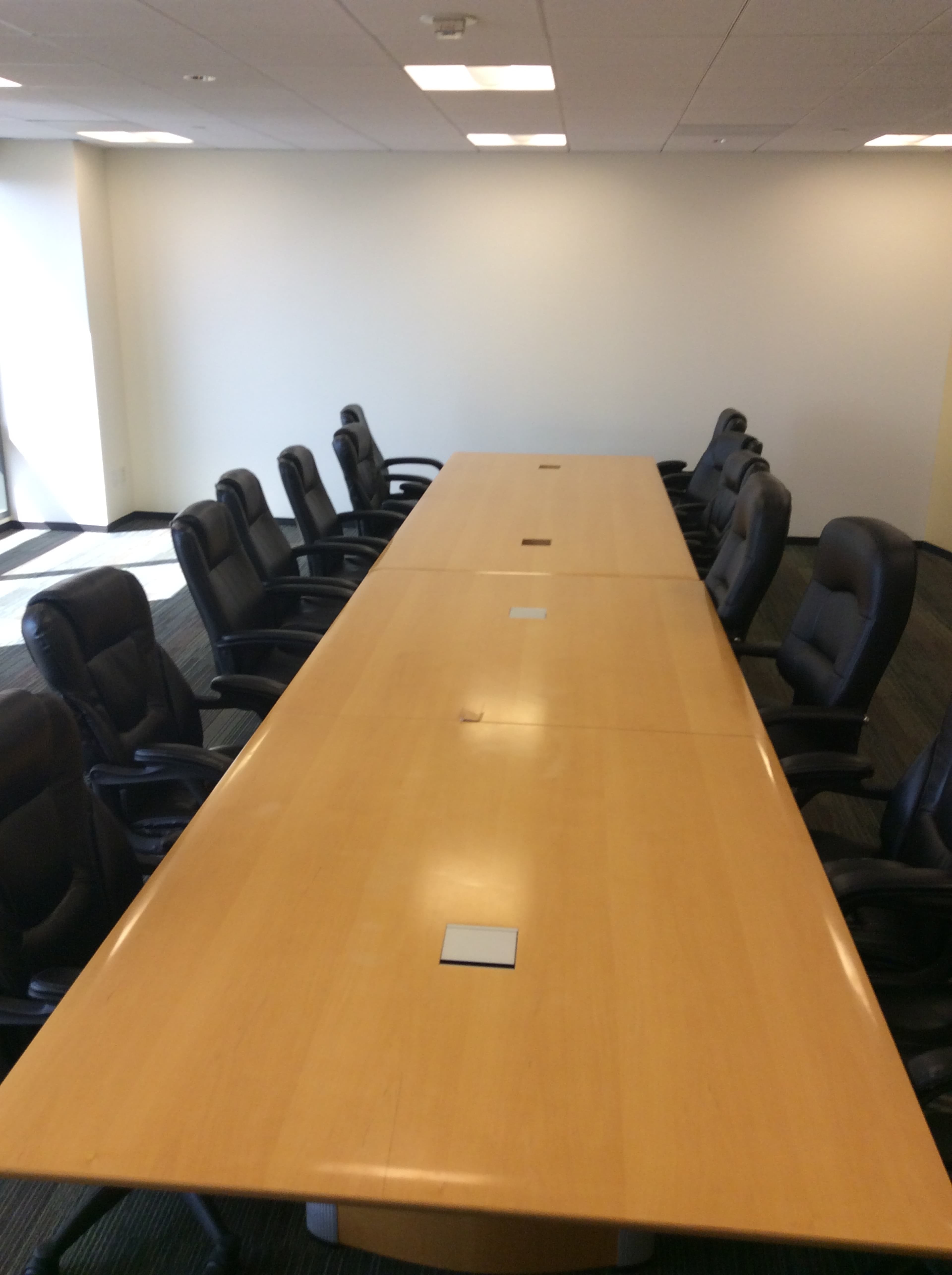 A long wooden conference table is surrounded by black office chairs in a well-lit meeting room.