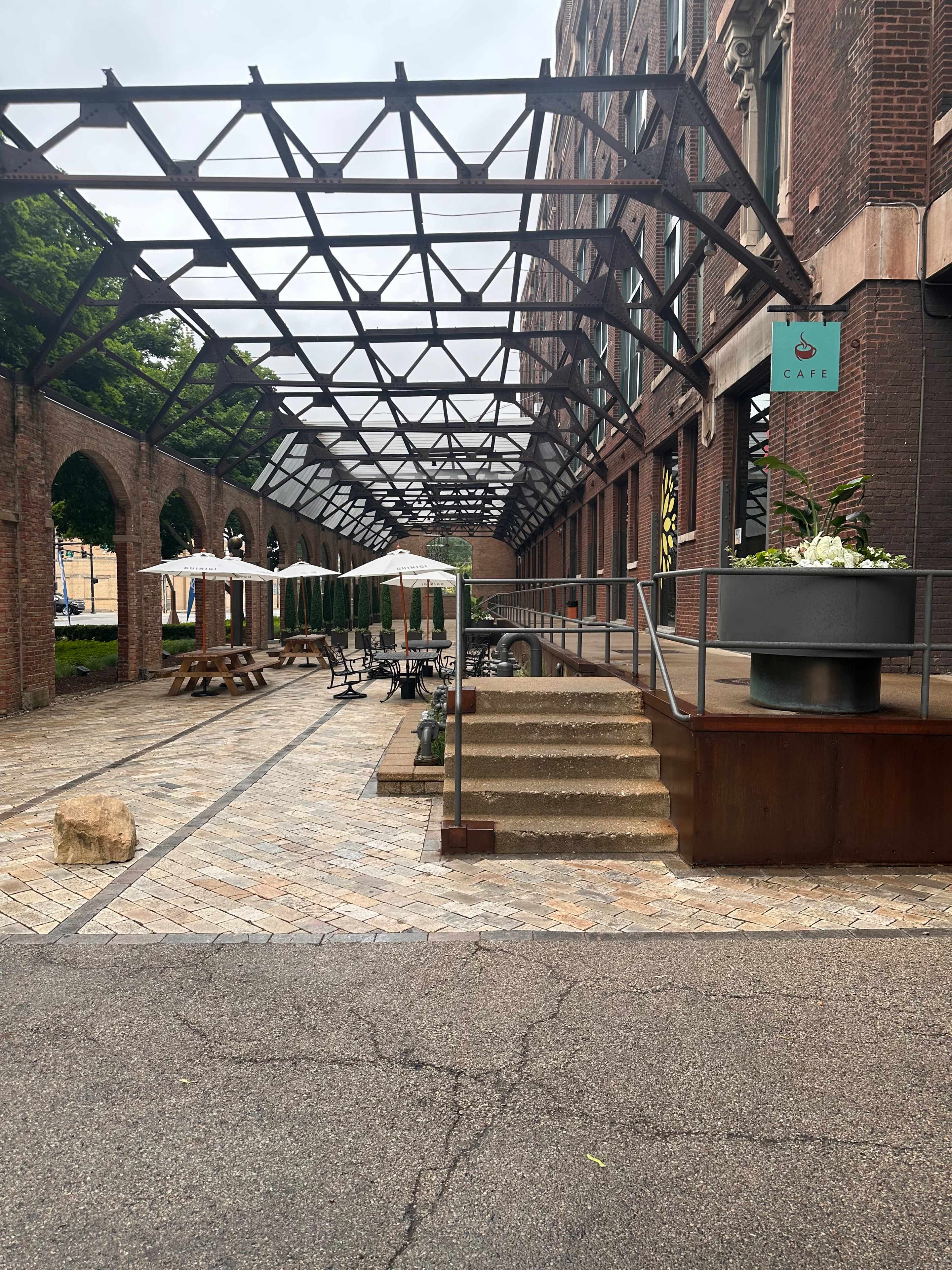 A covered walkway lined with brick walls and stone pavement, leading to a café entrance.