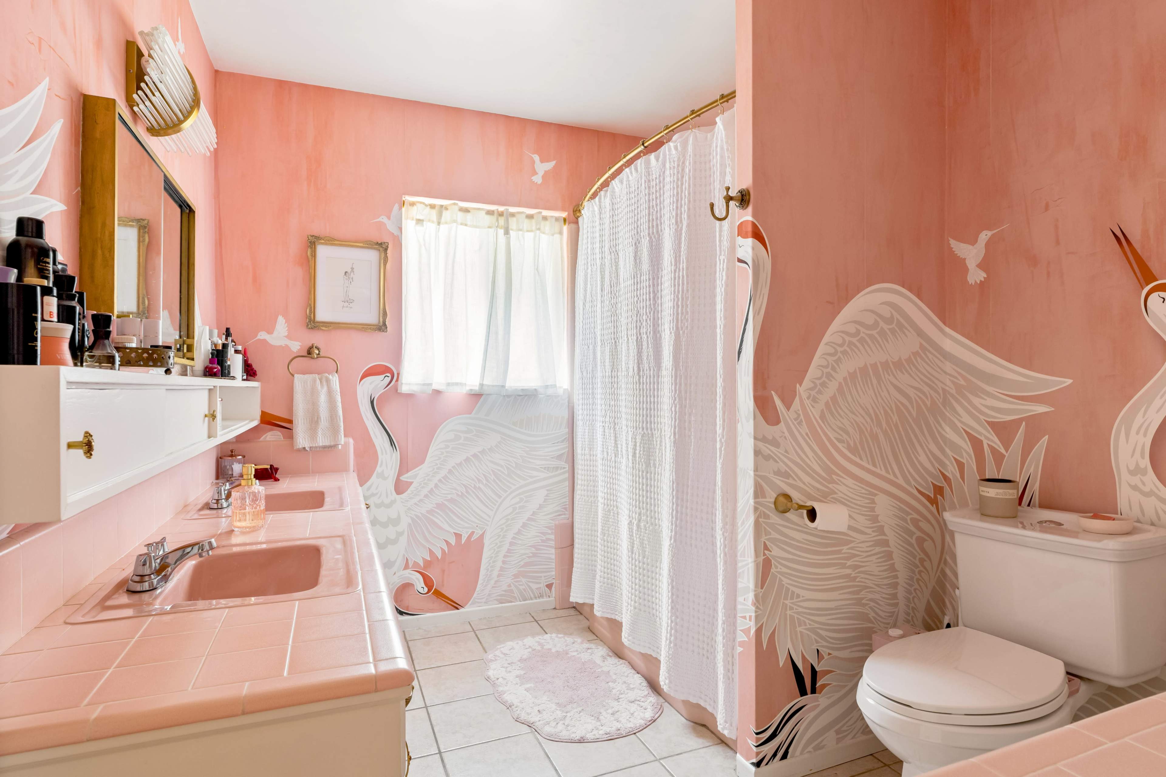 The bathroom features pink walls with white swan murals and a shower curtain, along with two sinks and a toilet.