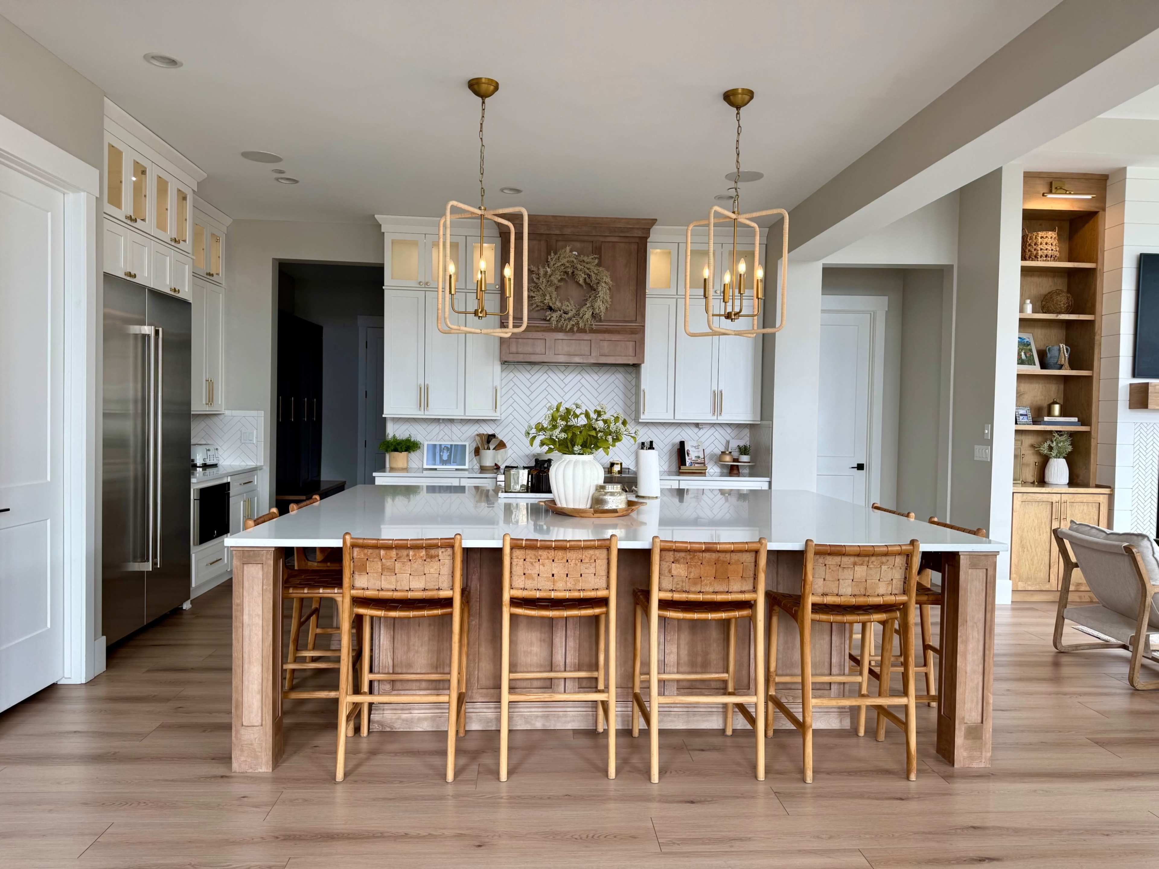 A spacious modern kitchen features a large central island with seating for eight, surrounded by white cabinetry and wood accents.
