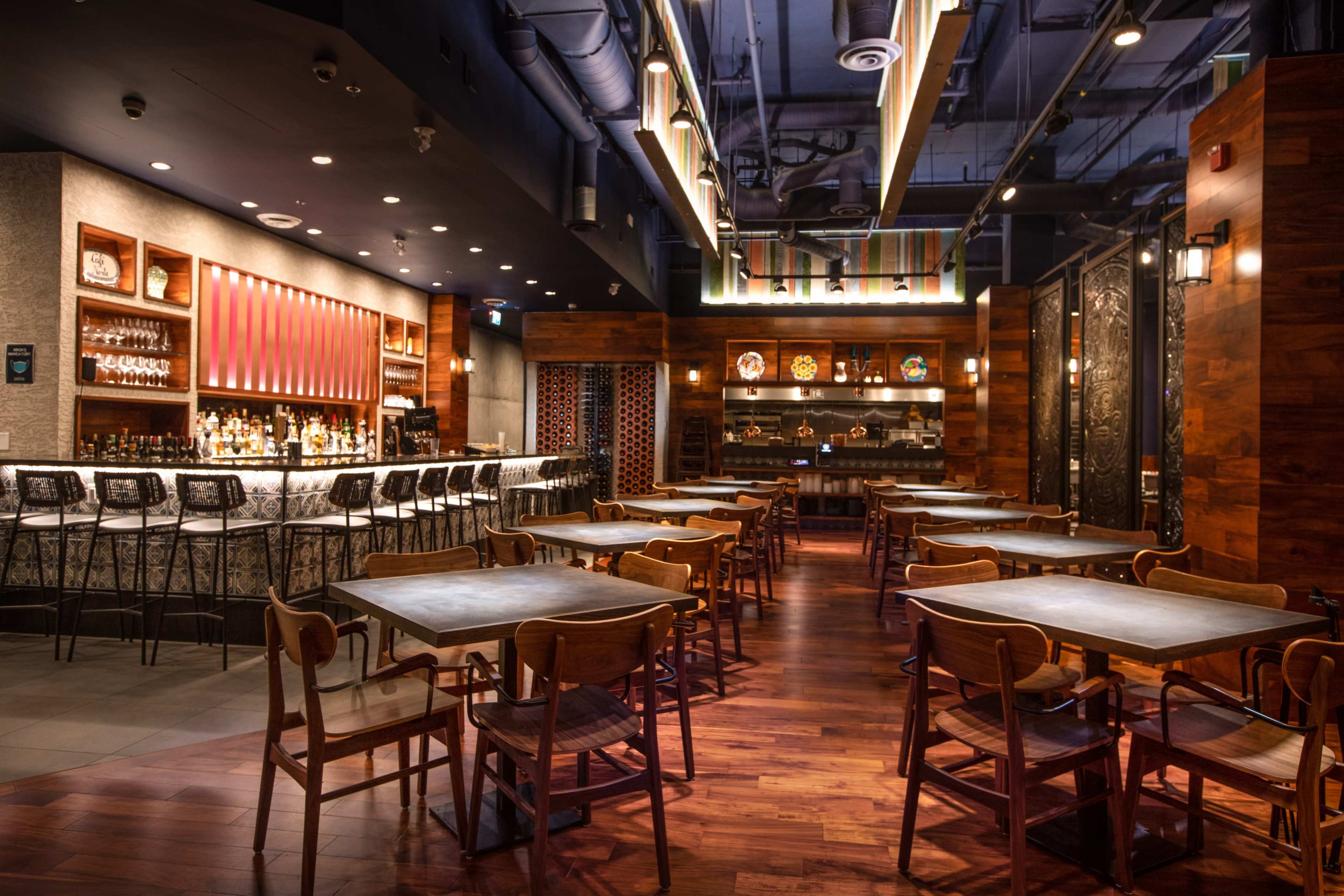 A spacious restaurant interior with a bar area on one side, wooden tables, and chairs arranged throughout the room.
