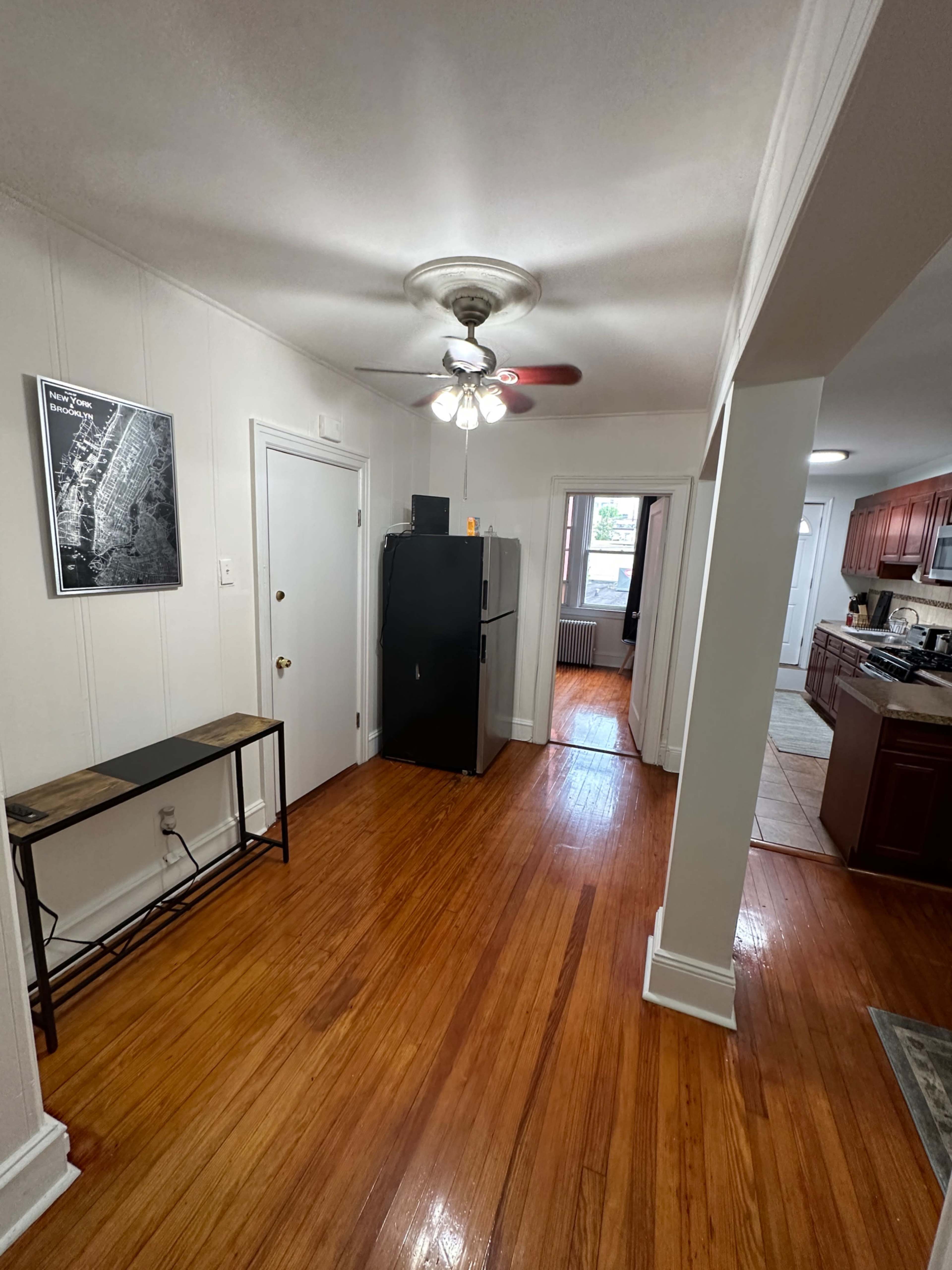 A narrow hallway in a home with a black refrigerator, a small table, and entryways leading to other rooms.