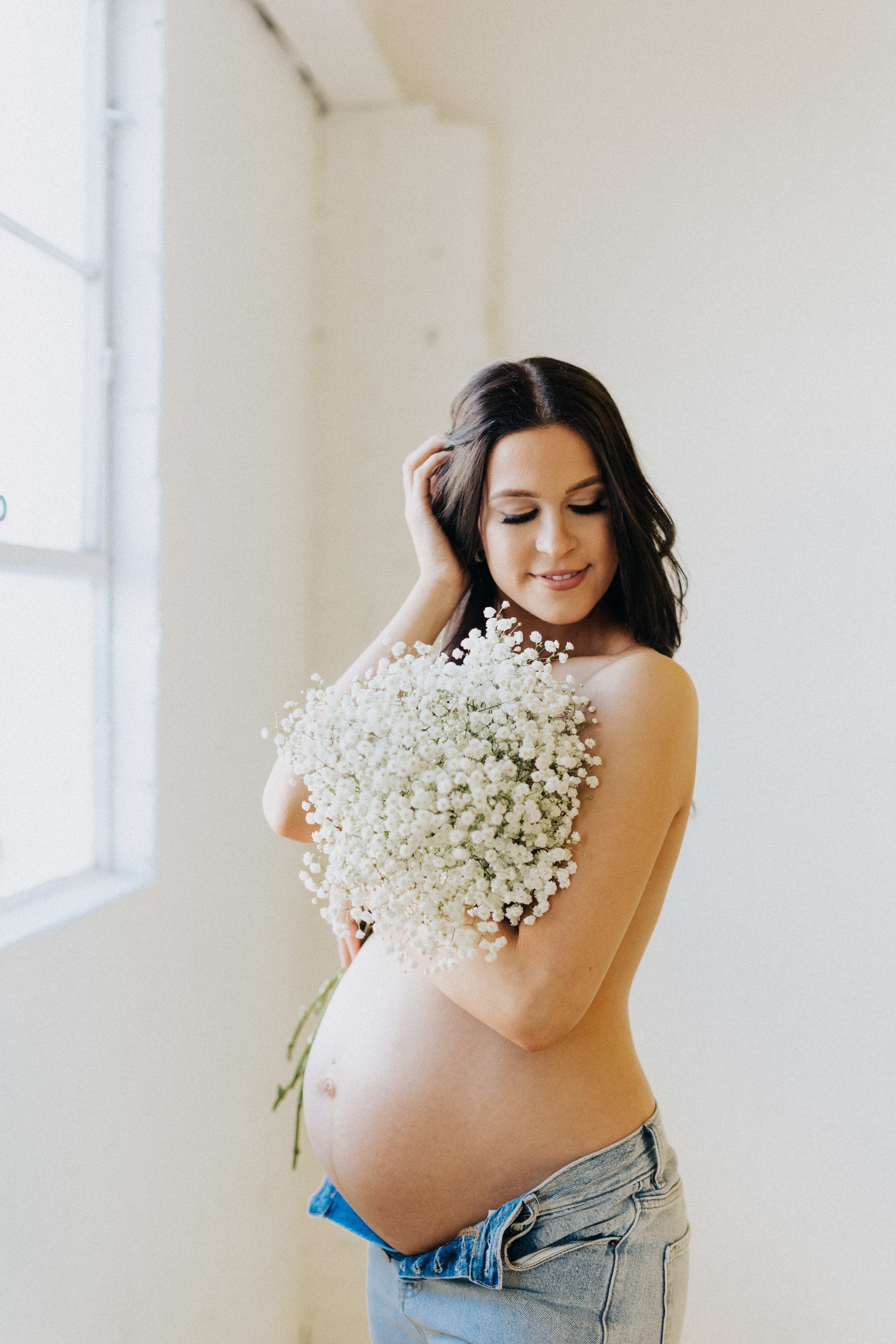 A maternity photo shoot with a pregnant woman holding white flowers.