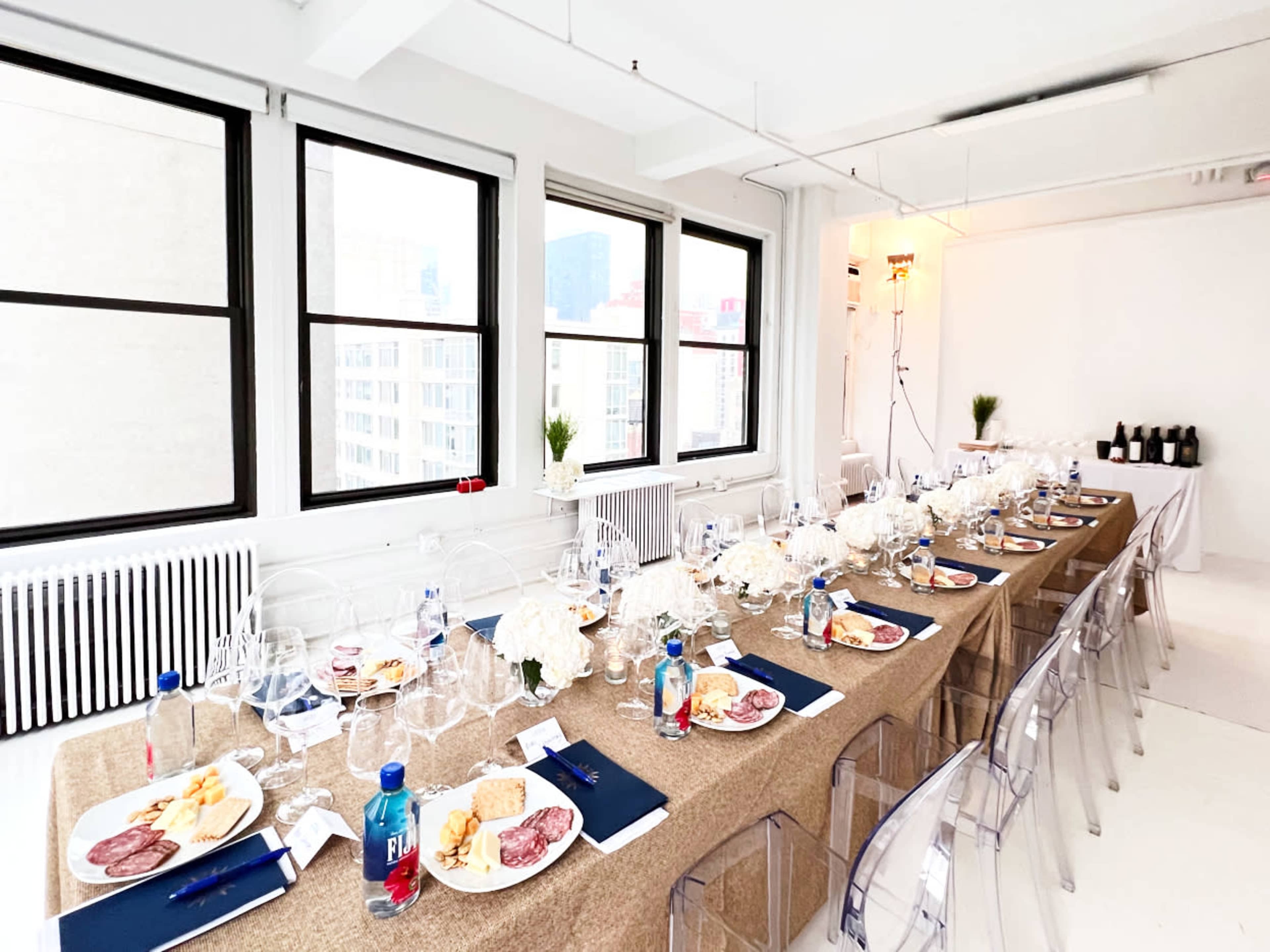 A long dining table is set with plates of food, glasses, and decorative elements in a bright, modern space with large windows.