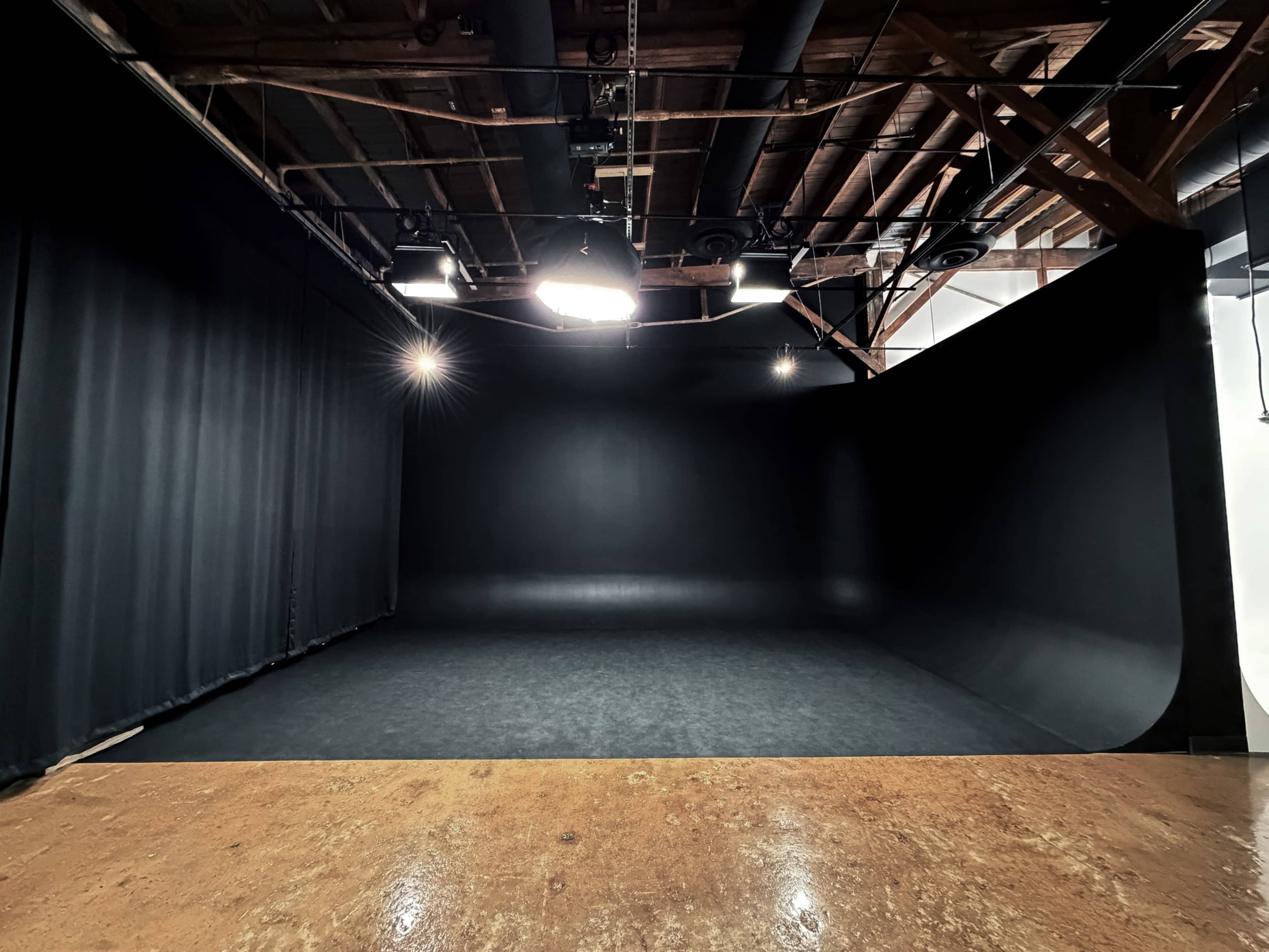 The image shows a spacious, dimly lit studio with a black backdrop and a wooden floor.