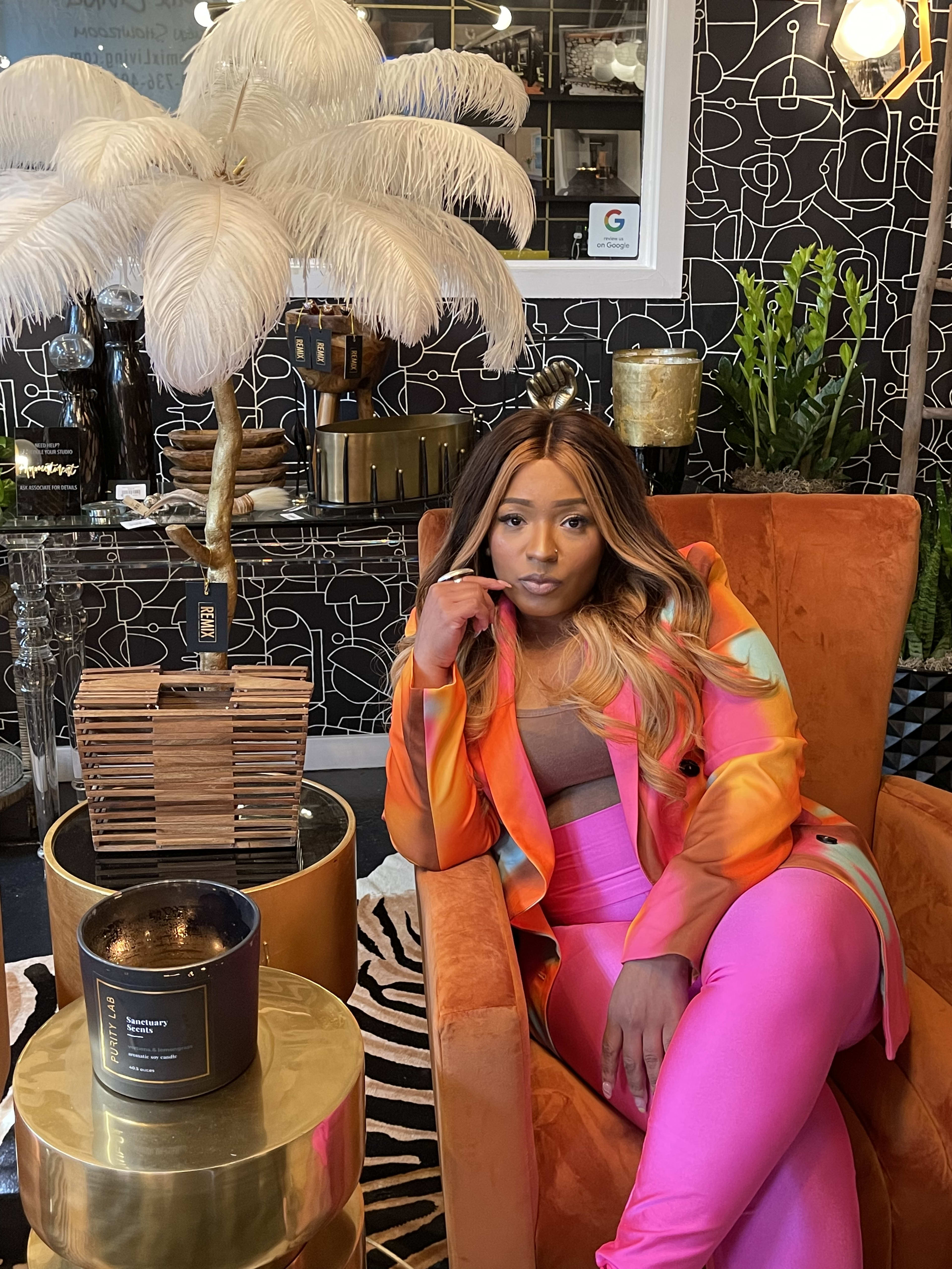 A fashionable woman in a colourful dress posing next to a display of art objects.