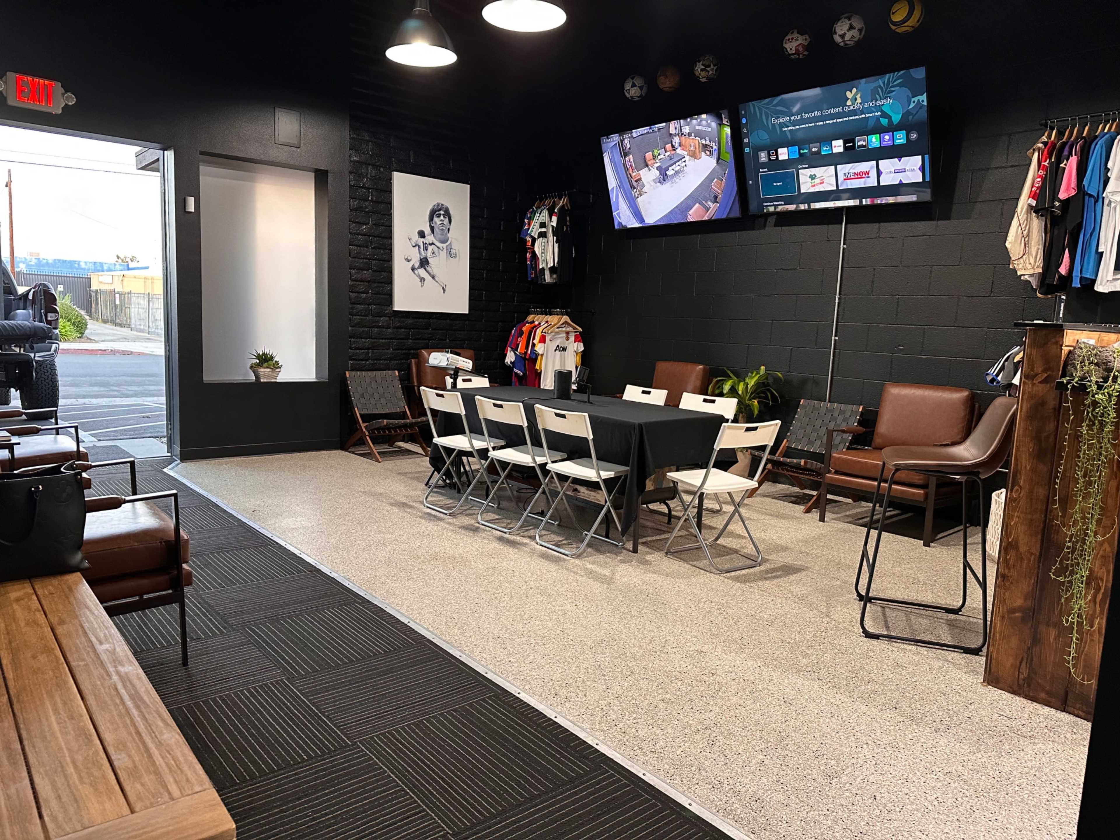 A spacious, modern room with a large table and chairs, a television on the wall, and racks of clothing displayed.