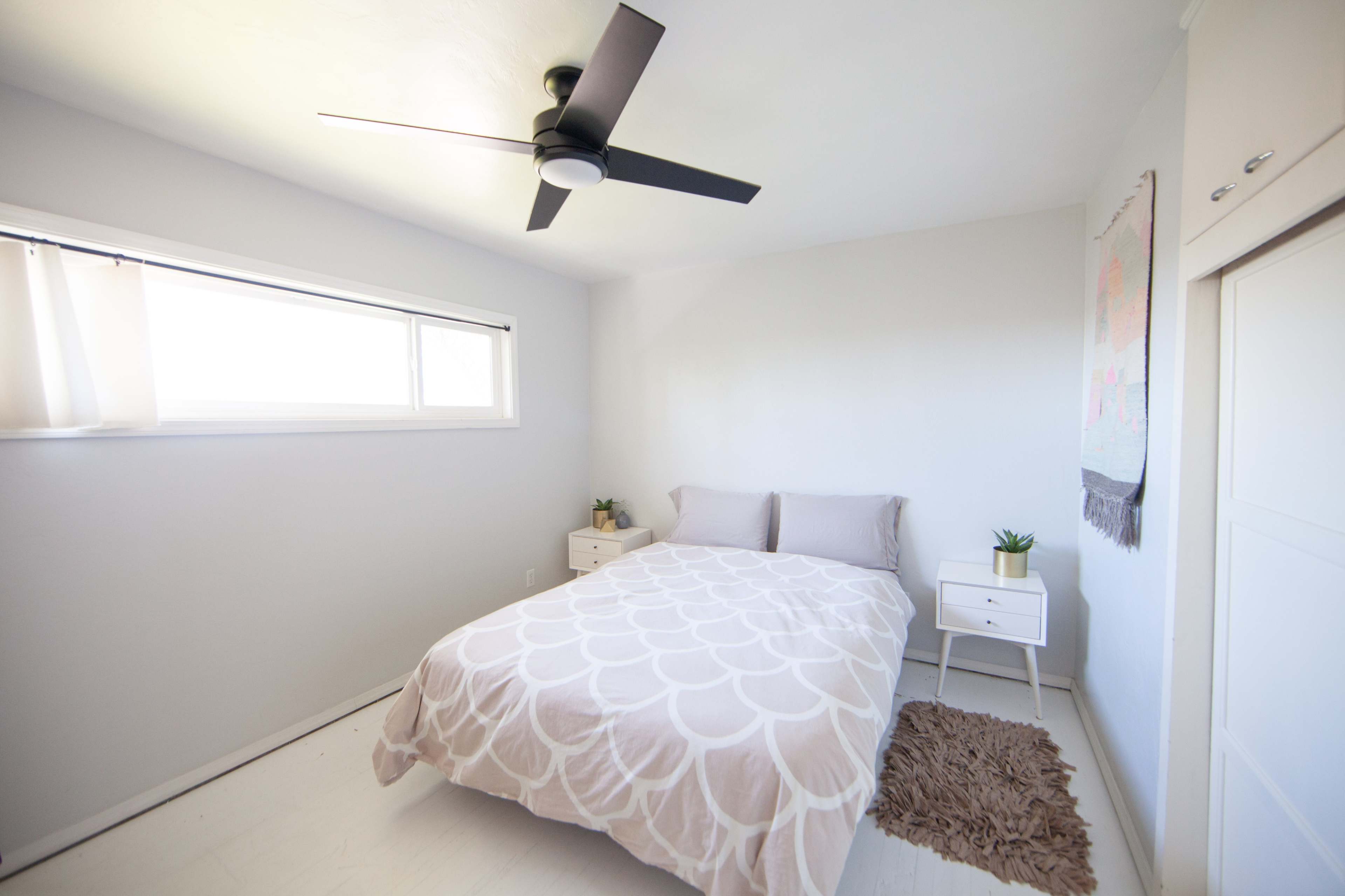 A minimalist bedroom with a bed, nightstands, and a window letting in natural light.
