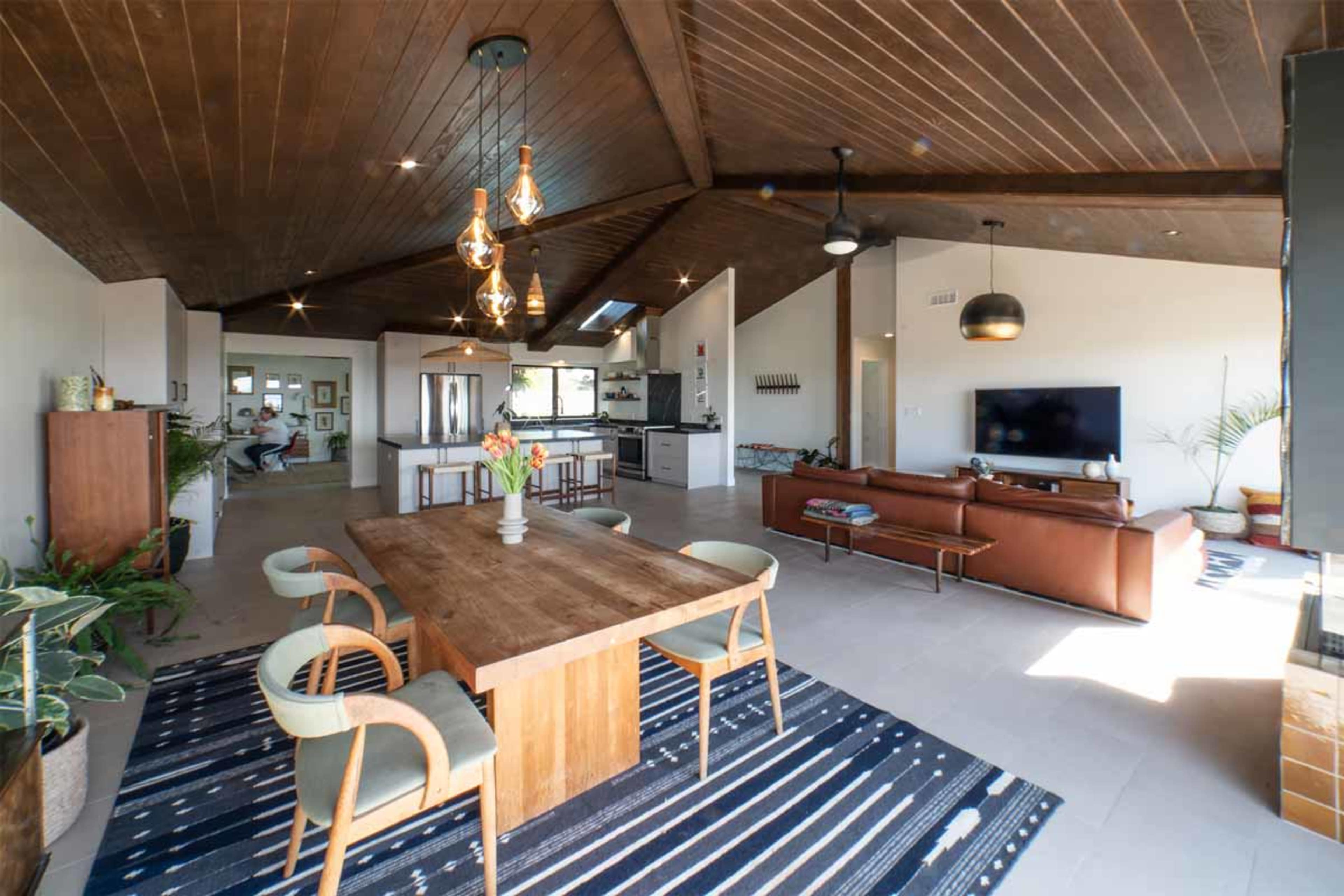 A modern interior featuring an open-concept living space with a dining table, leather sofa, and a kitchen in the background.