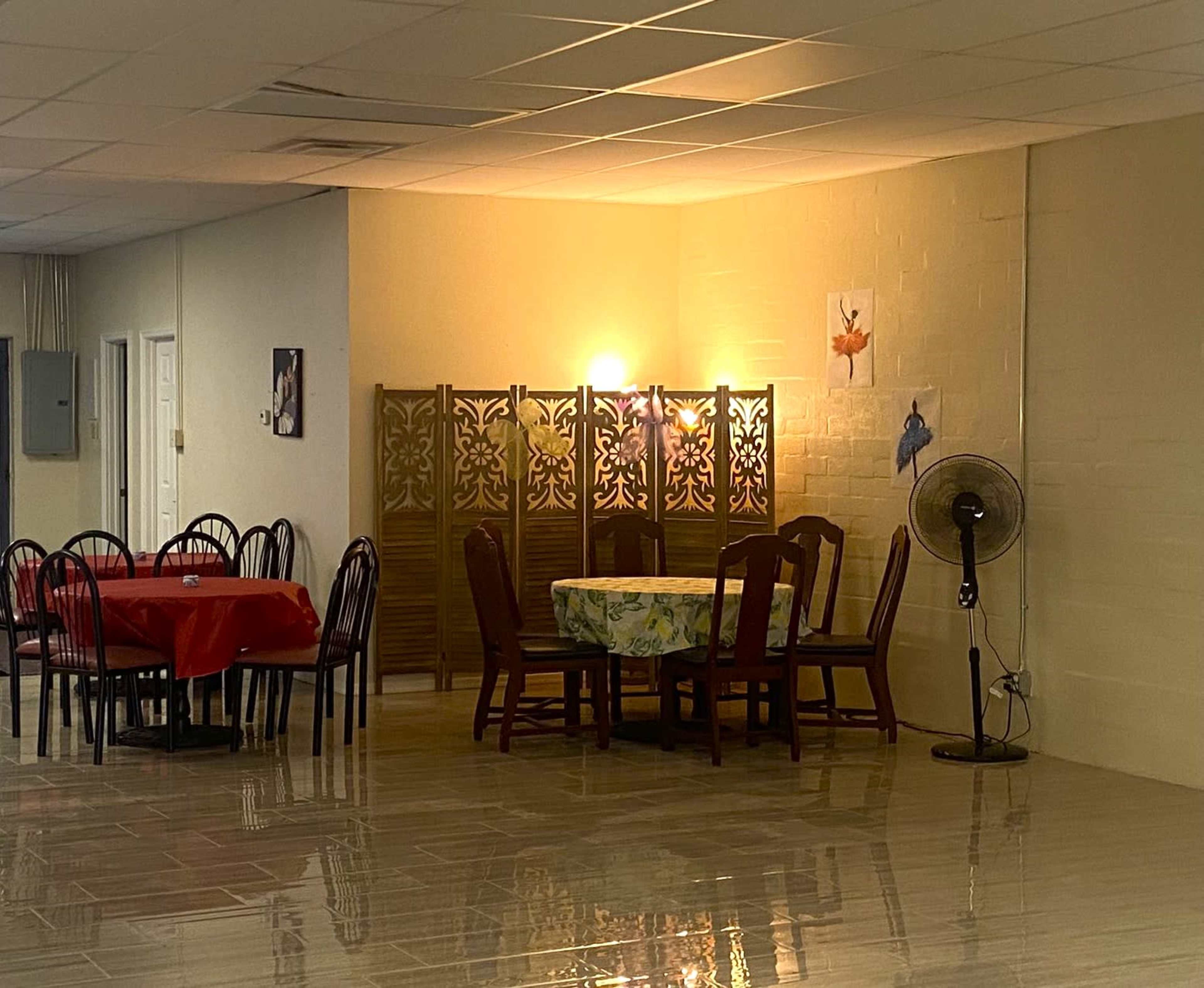 A dining area with tables and chairs, a decorative folding screen, and a fan in a well-lit room.
