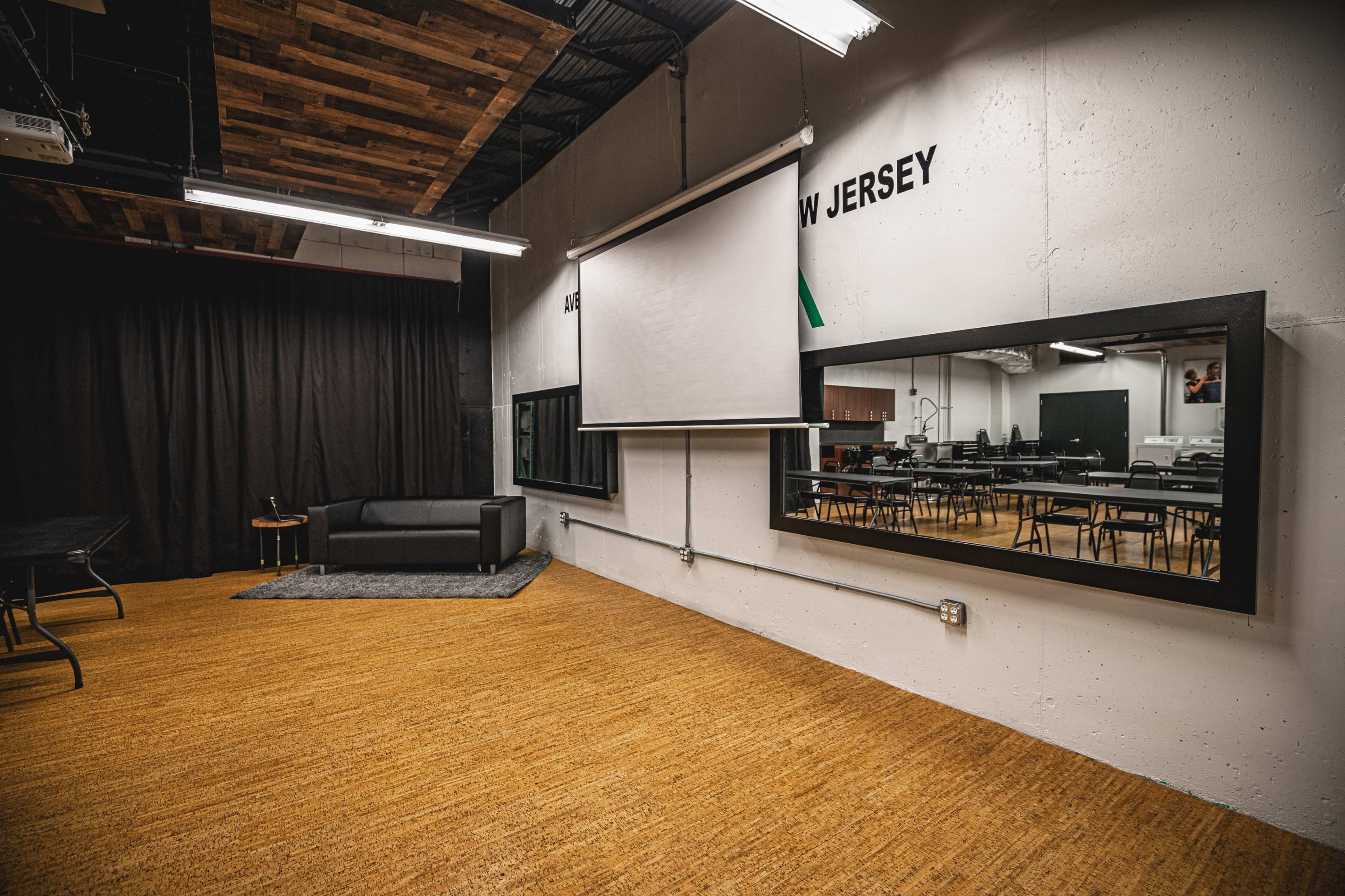 A spacious classroom or workshop area with a black sofa, a large mirror, and multiple tables arranged for use.