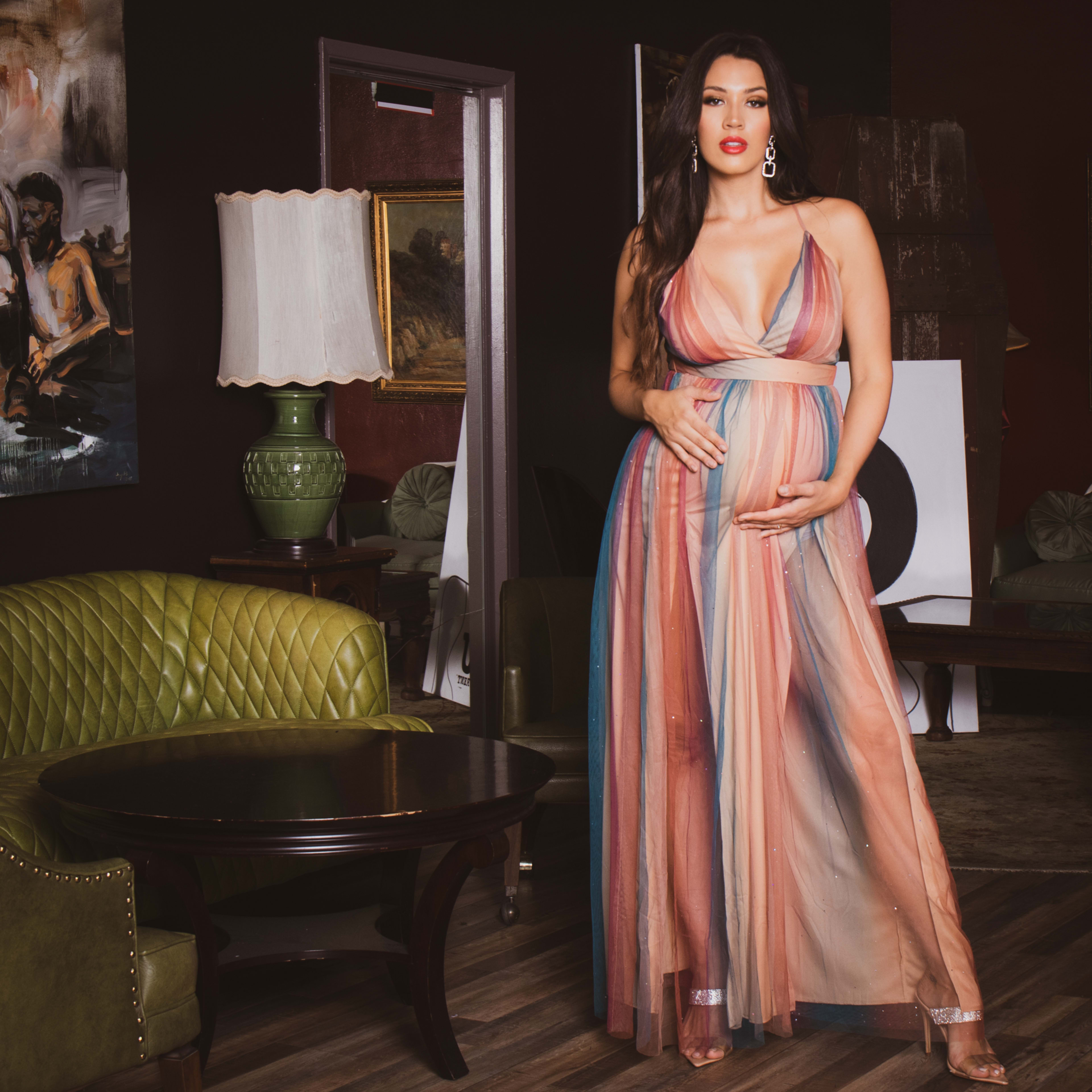 A maternity photo shoot of a woman in a dress holding her belly in a sitting room.