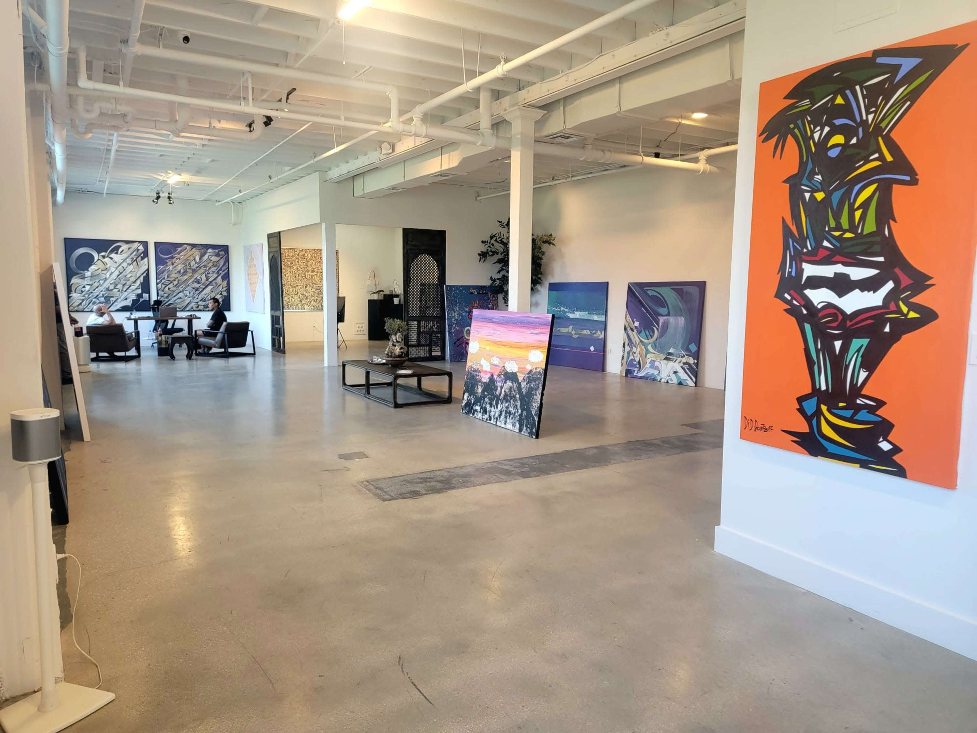 An art gallery with various paintings displayed on the walls and a seating area in the background.
