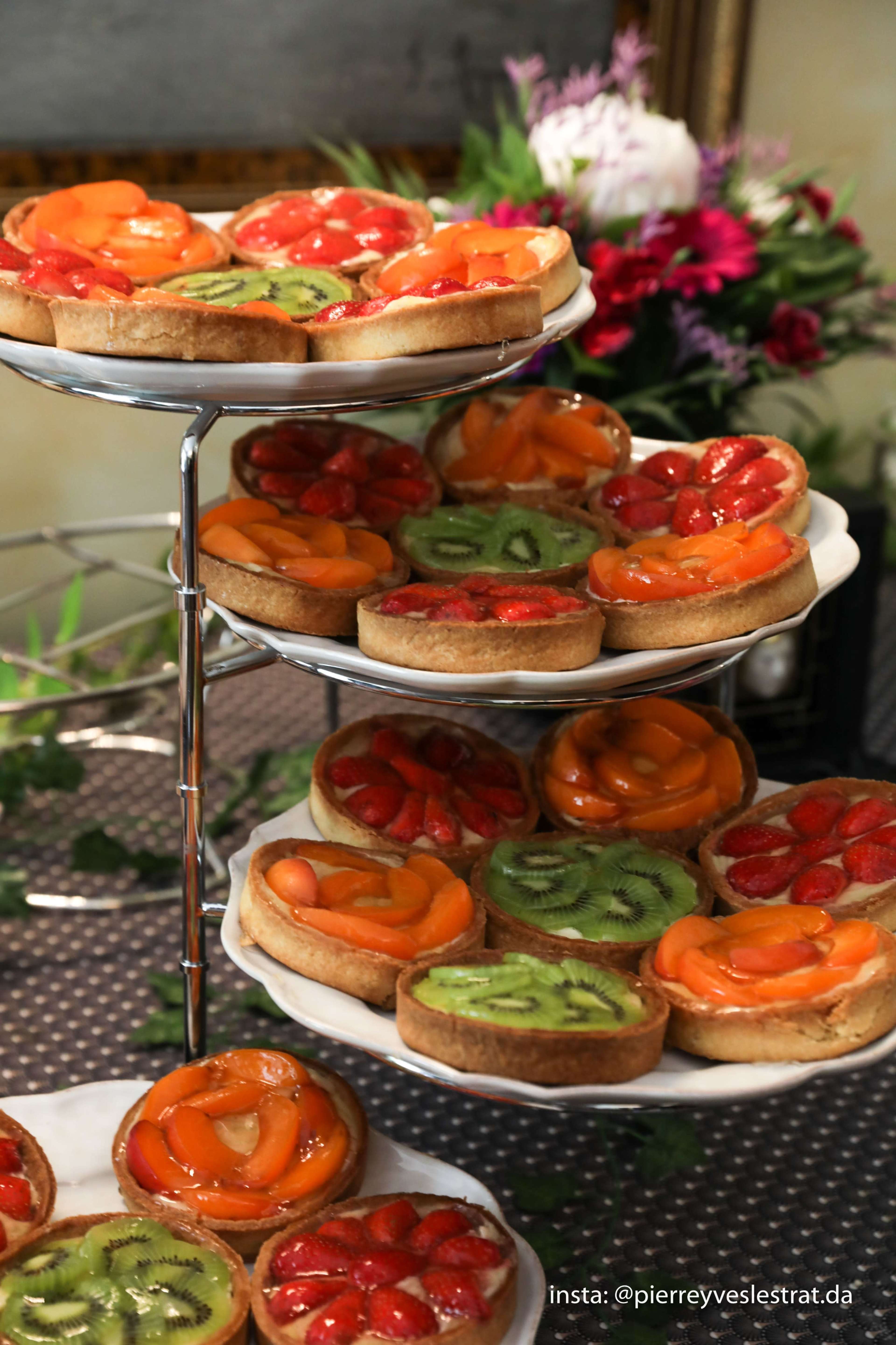 The image features three tiers of fruit tarts, each topped with colorful slices of various fruits, including orange, kiwi, strawberry, and peach.