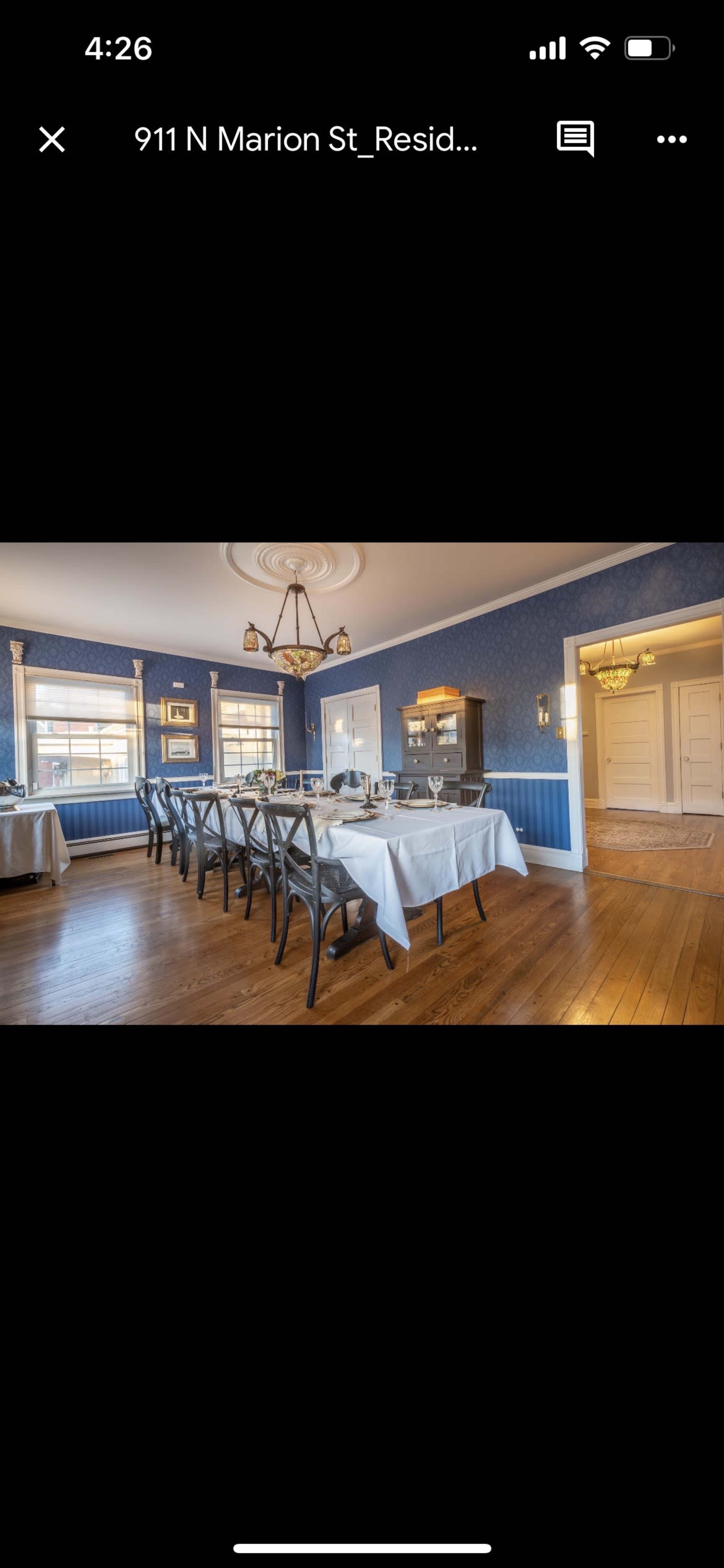 A dining room with a long table set for several guests, featuring blue walls and wooden flooring.