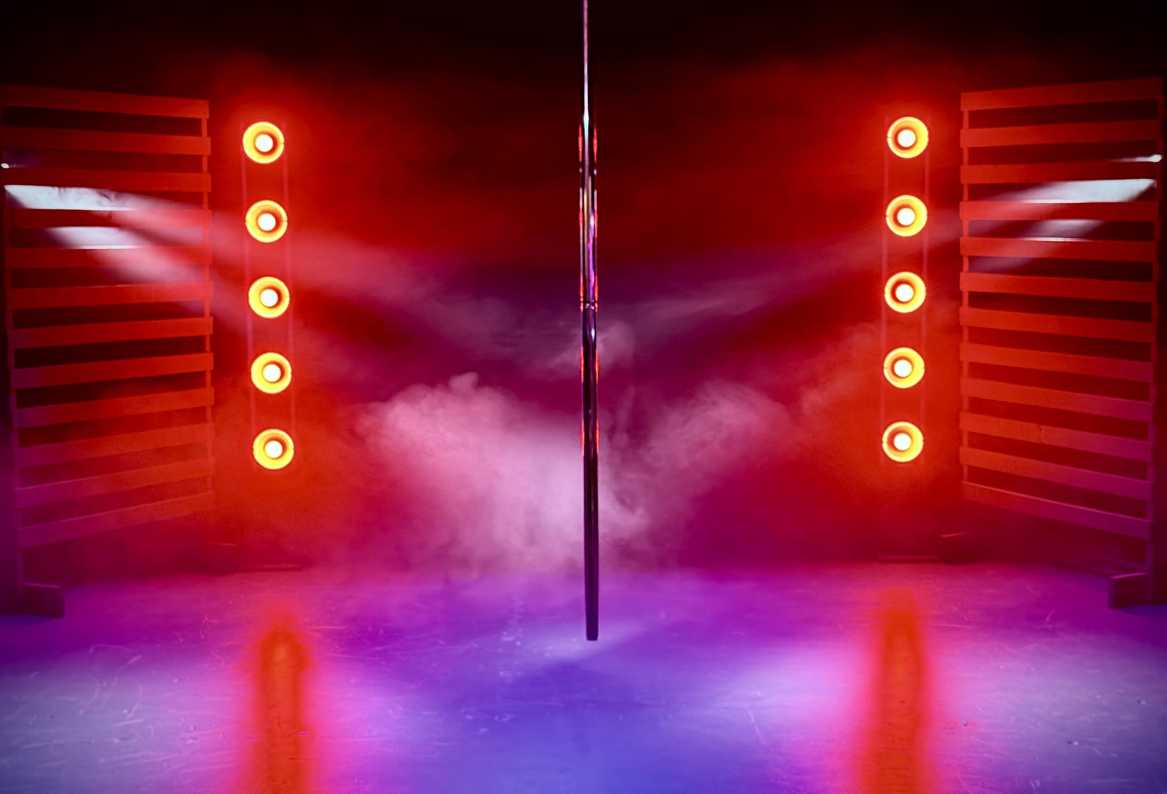 The image shows a dimly lit stage with a vertical pole surrounded by red lights and smoke effects.