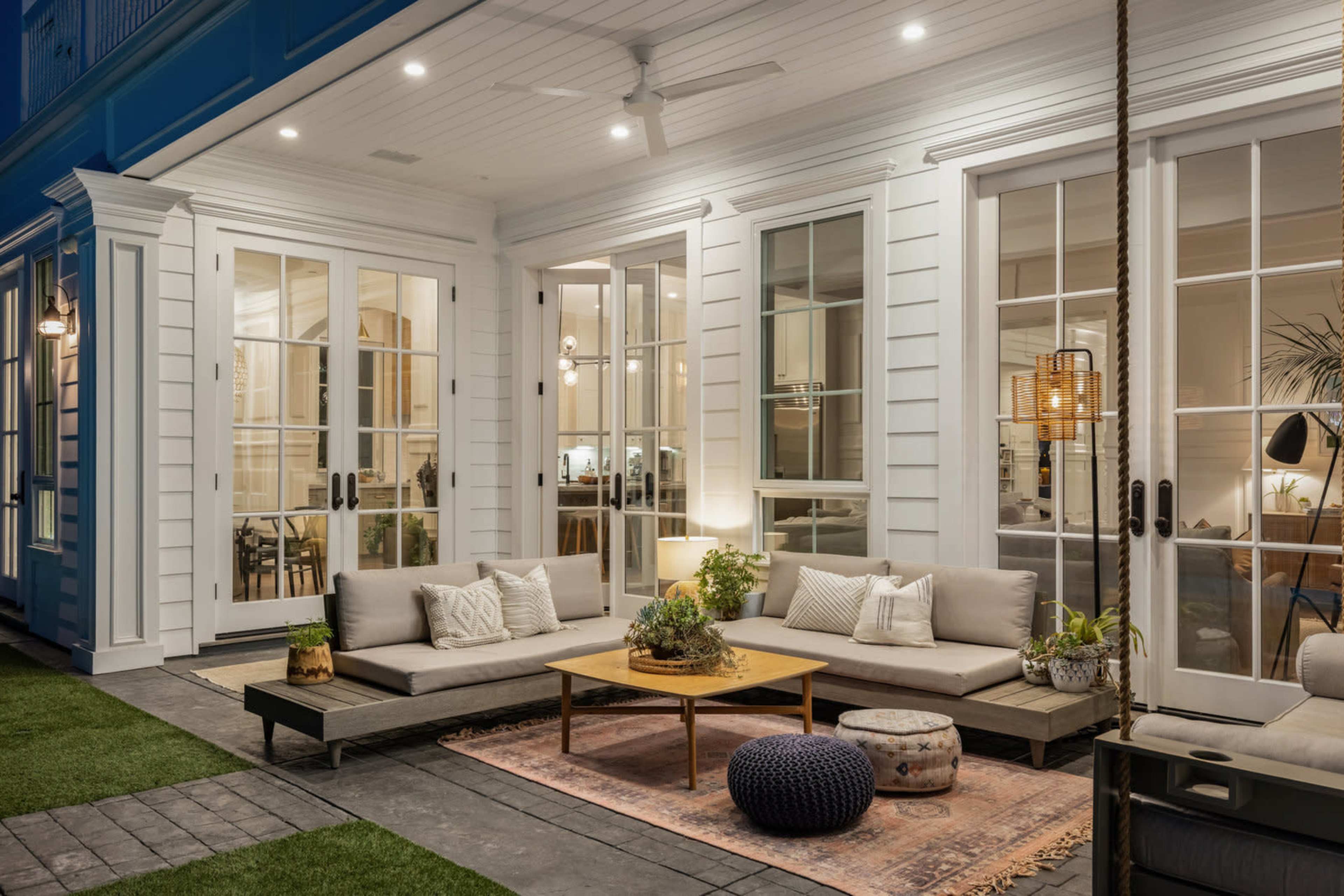 A modern outdoor seating area features a low couch, wooden coffee table, decorative cushions, and potted plants, illuminated by ambient lighting.