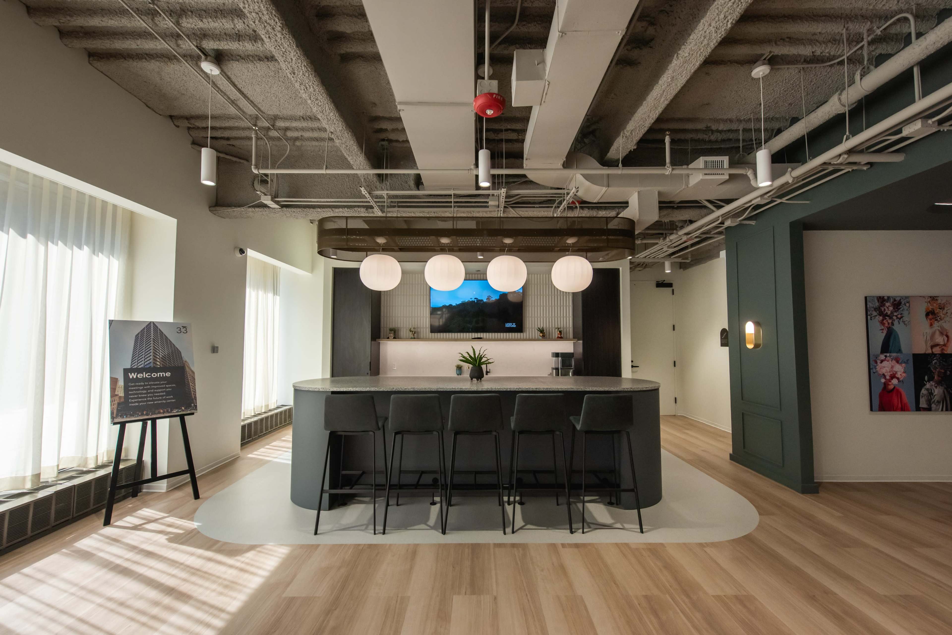 The image shows a modern reception area with a gray counter, three black stools, pendant lights, and a large window with natural light.