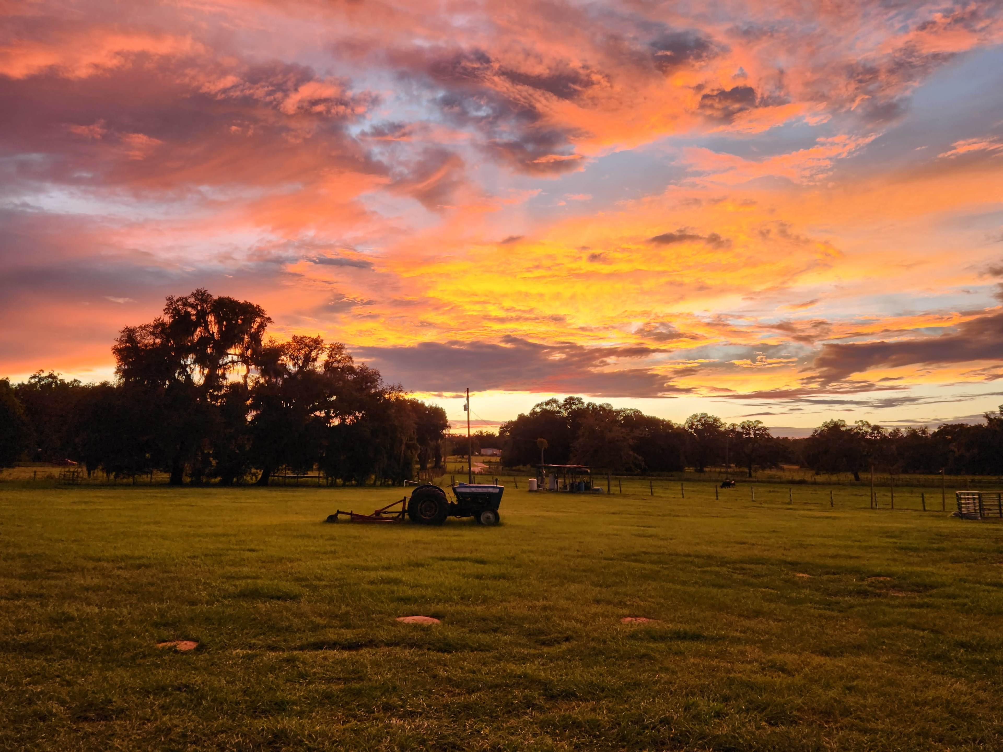 A tractor is parked in a grassy field under a vibrant sunset with colorful clouds.