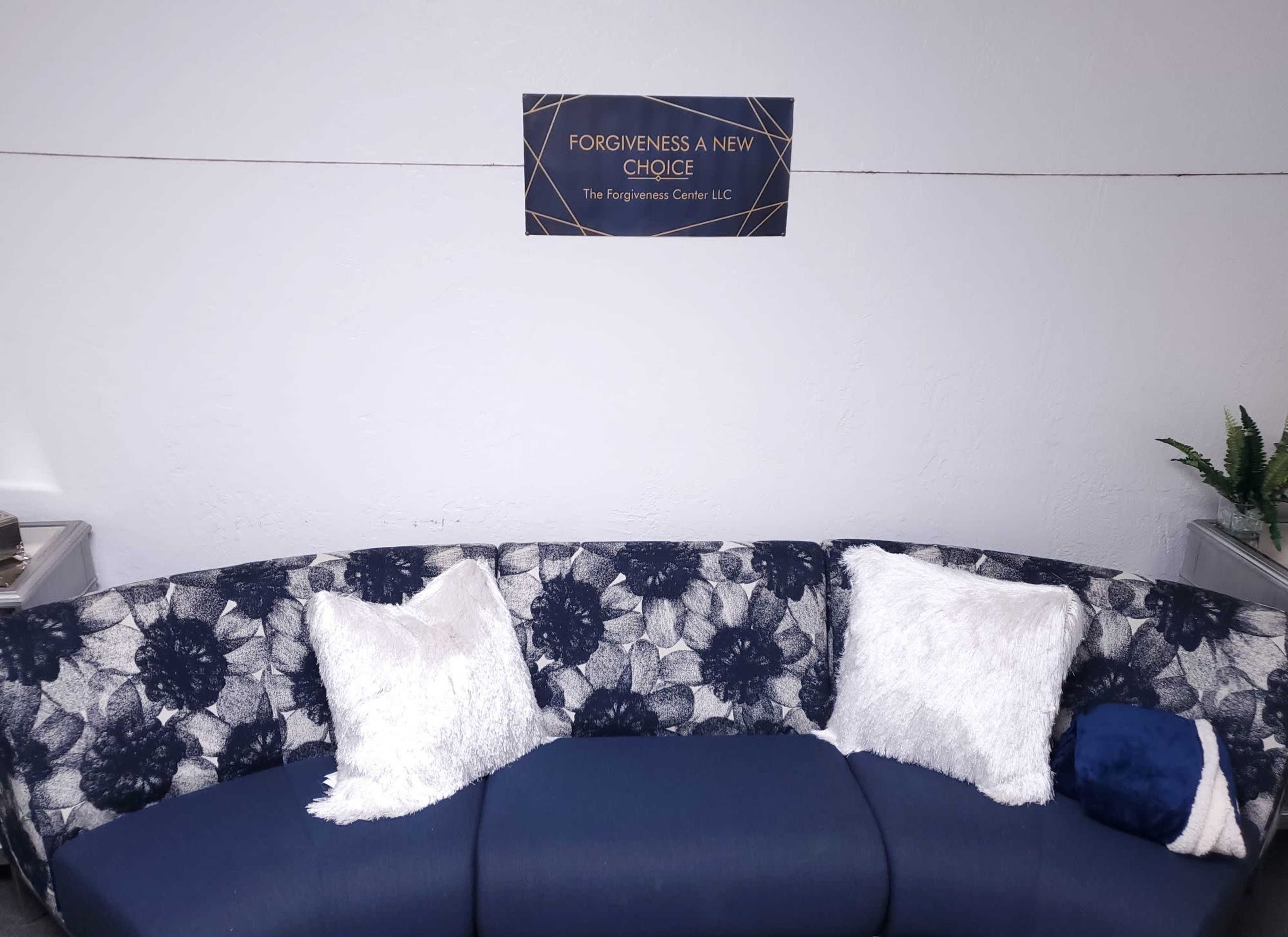 A curved couch with decorative pillows and a wall sign that reads "FORGIVENESS A NEW CHOICE" above it.