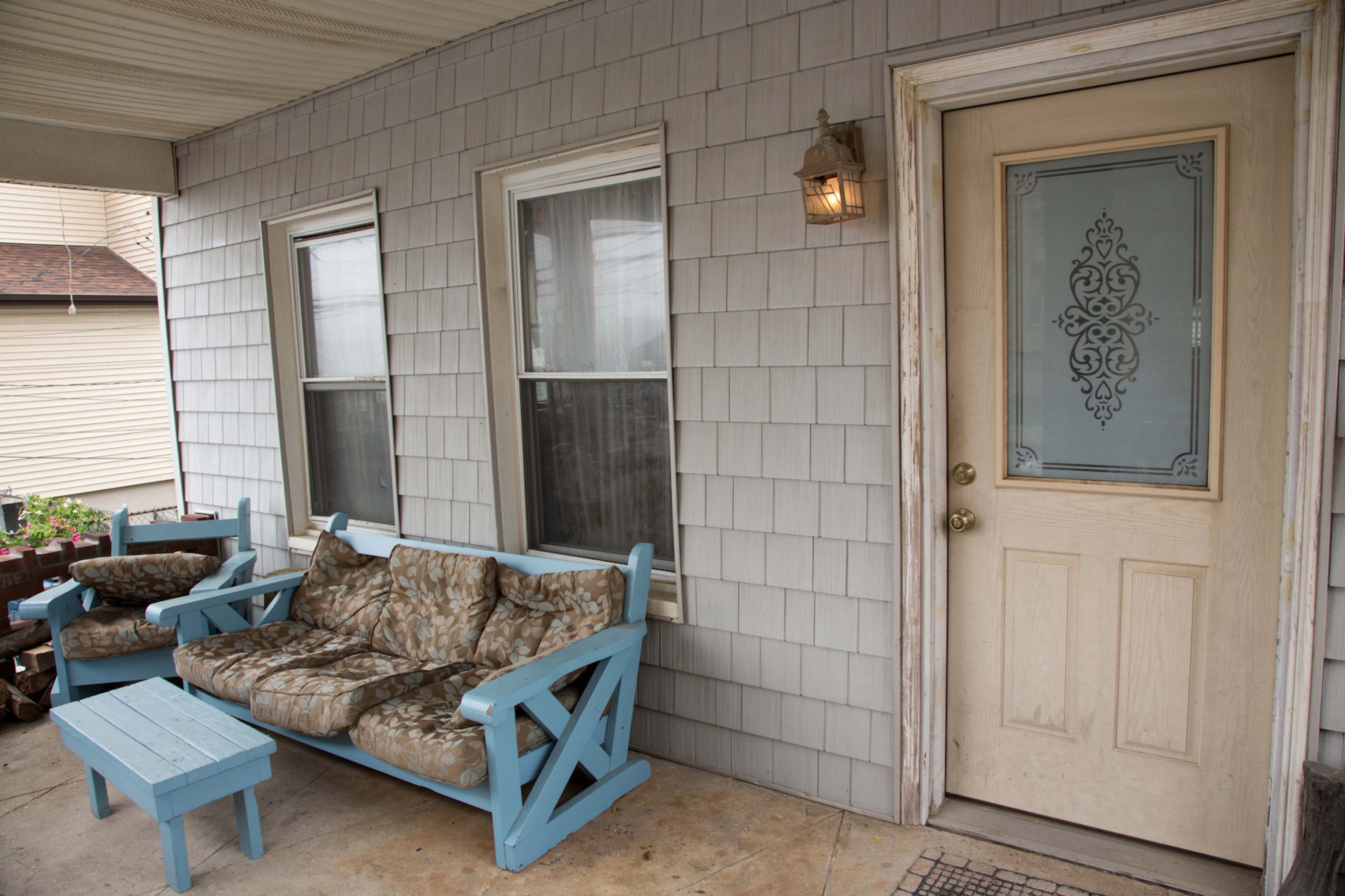 The image shows a porch with a light blue couch and a matching small table, situated in front of a door with decorative glass elements.
