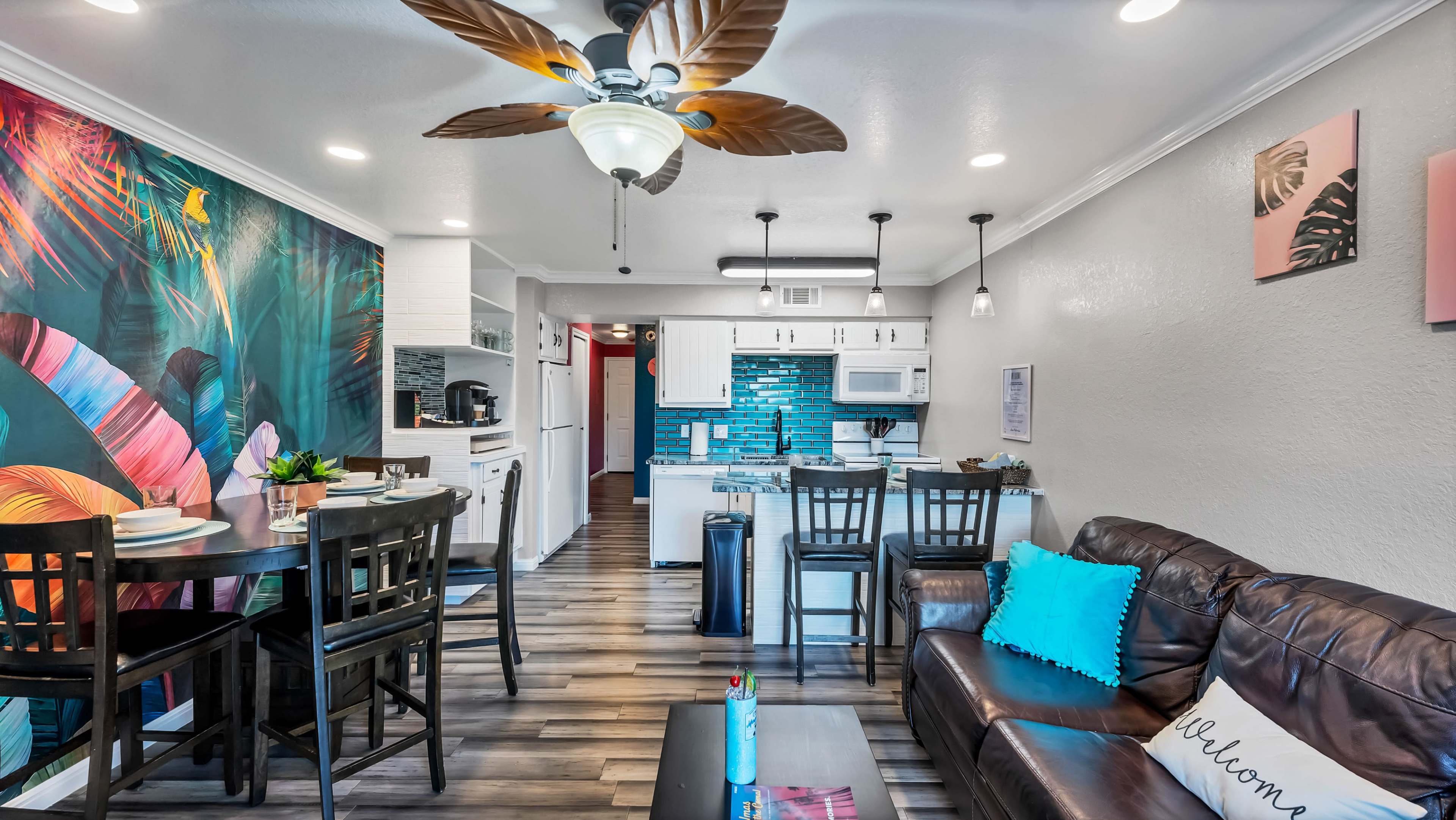 A modern living space featuring a kitchen, dining area, and comfortable seating with vibrant wall decor and wooden flooring.
