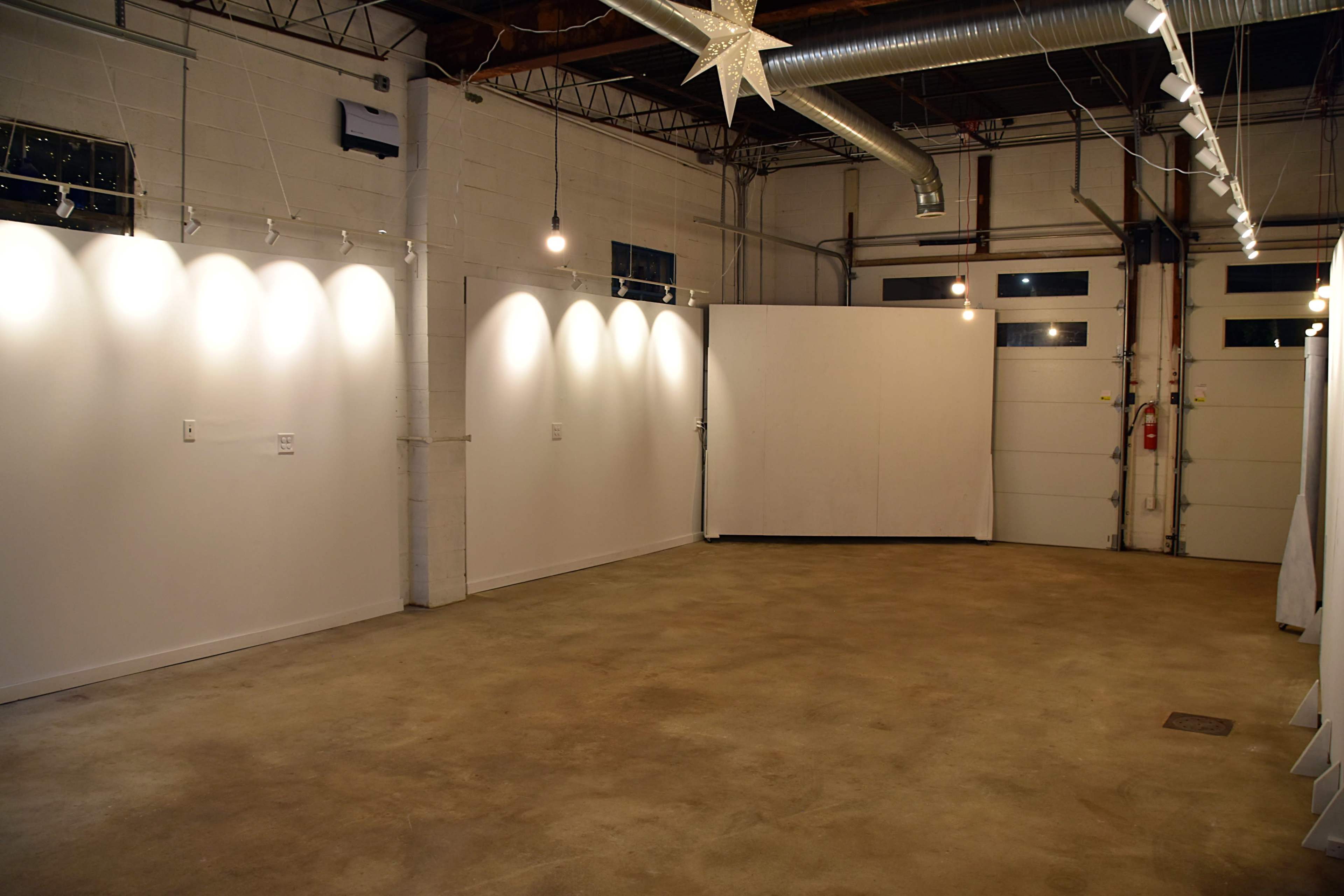 A spacious, empty gallery with white walls, polished concrete flooring, and overhead lighting.