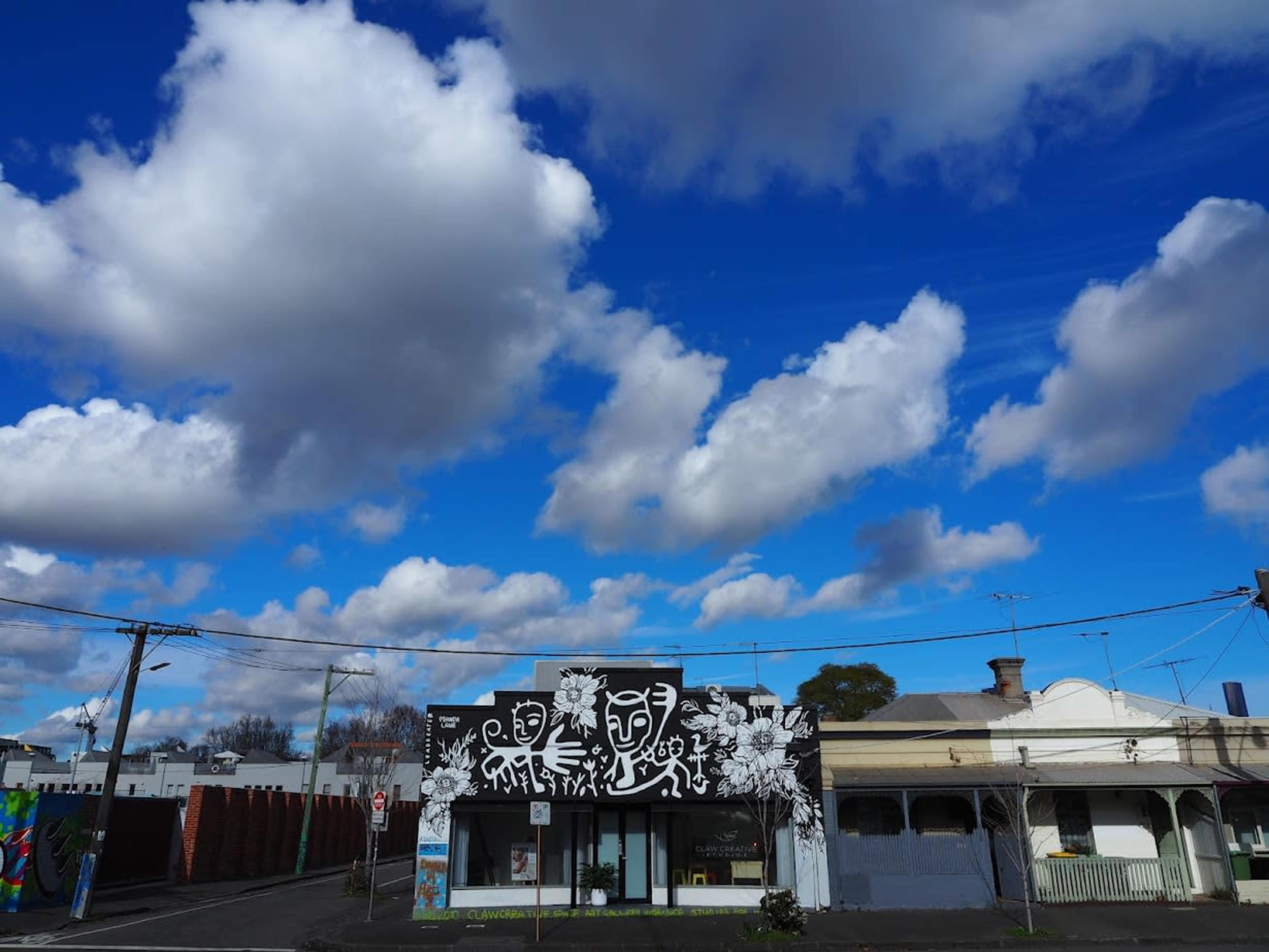 A storefront with a black and white mural under a sky filled with fluffy clouds is seen.