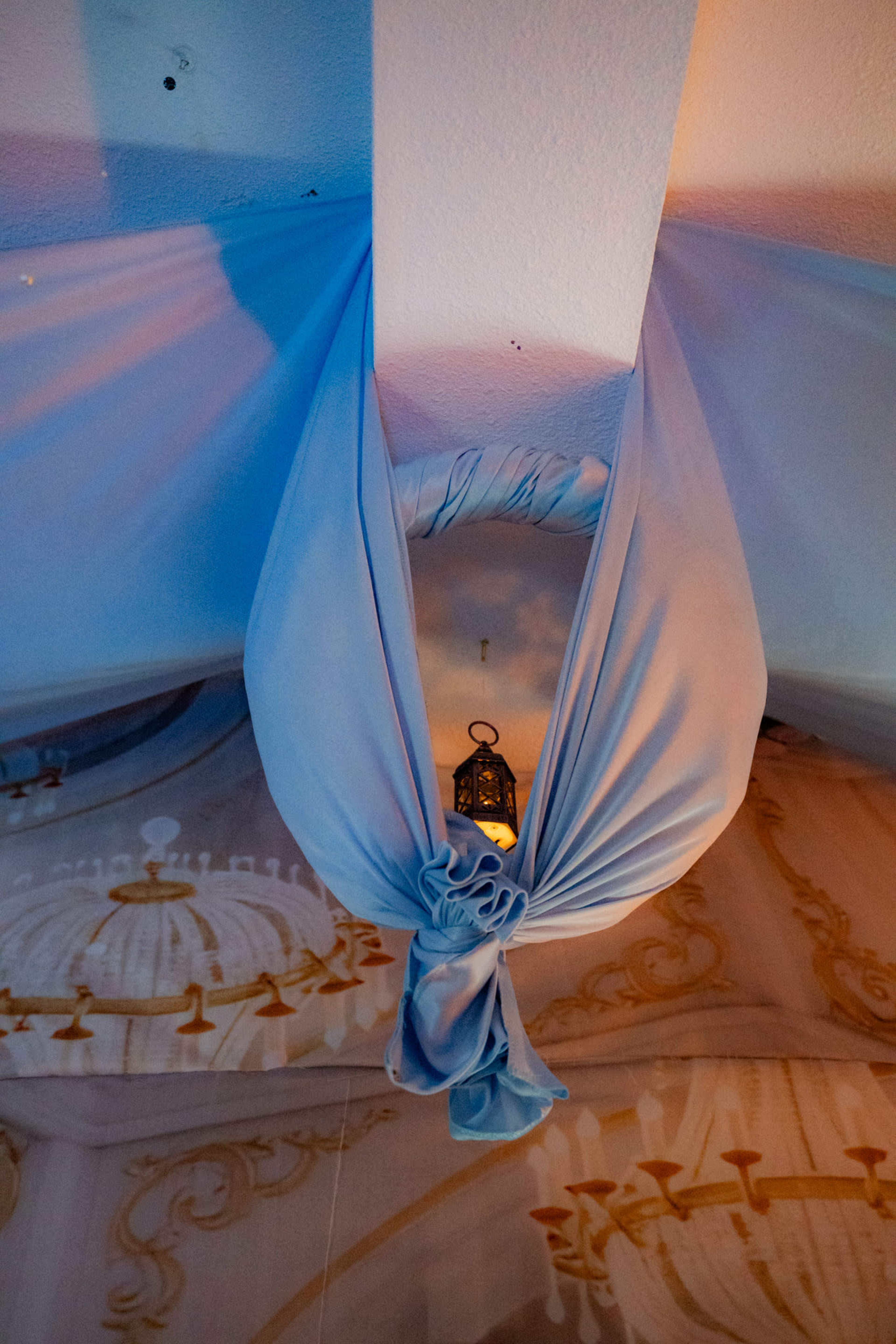 A blue fabric draped from the ceiling holds a lantern at its center within a decorated interior.