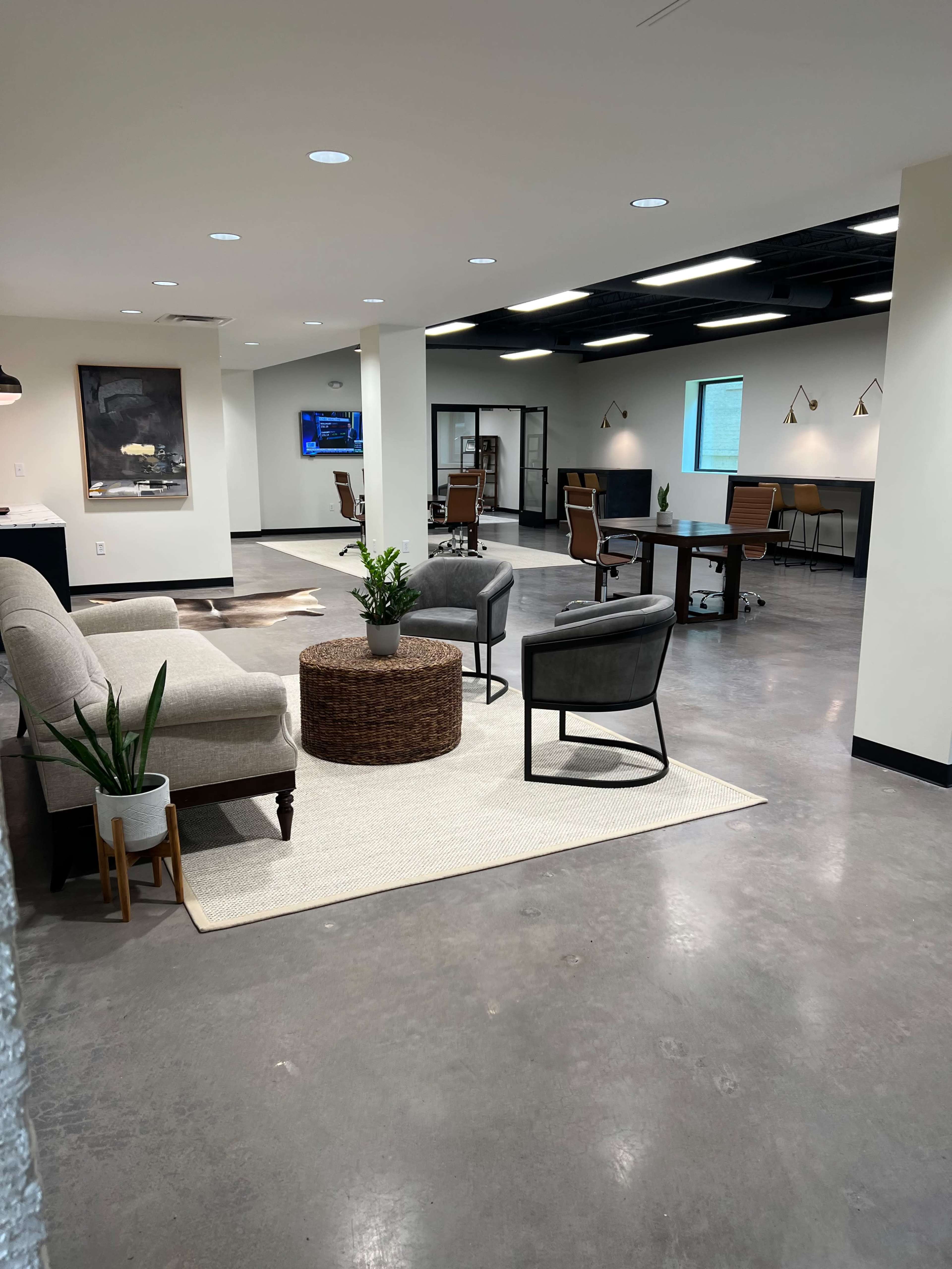 A modern office space with a seating area featuring gray chairs, a round table, and a rug, alongside workstations equipped with chairs and computers.
