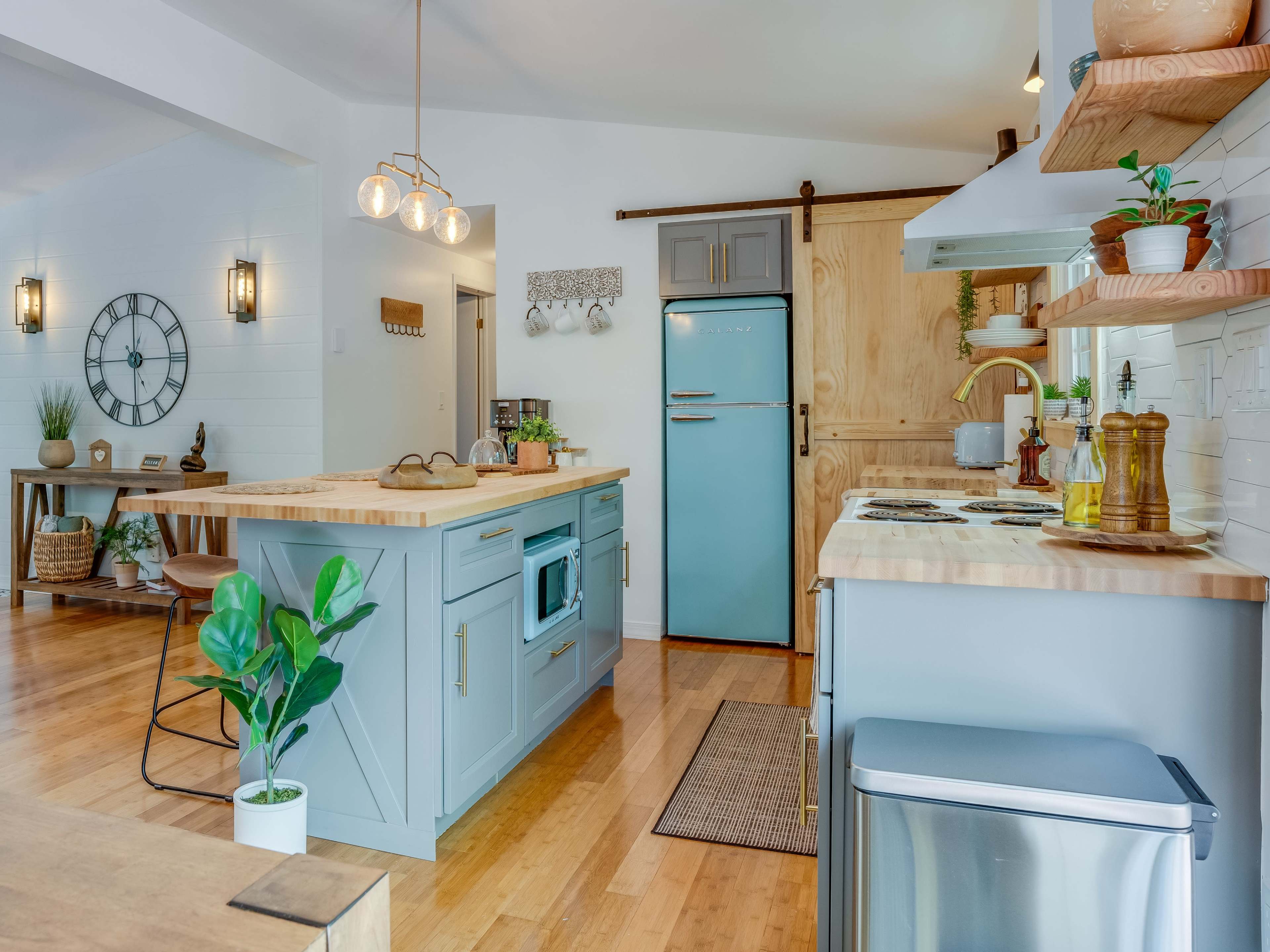 The image showcases a modern kitchen featuring a blue retro-style refrigerator, wooden countertops, and a spacious island with a sink.