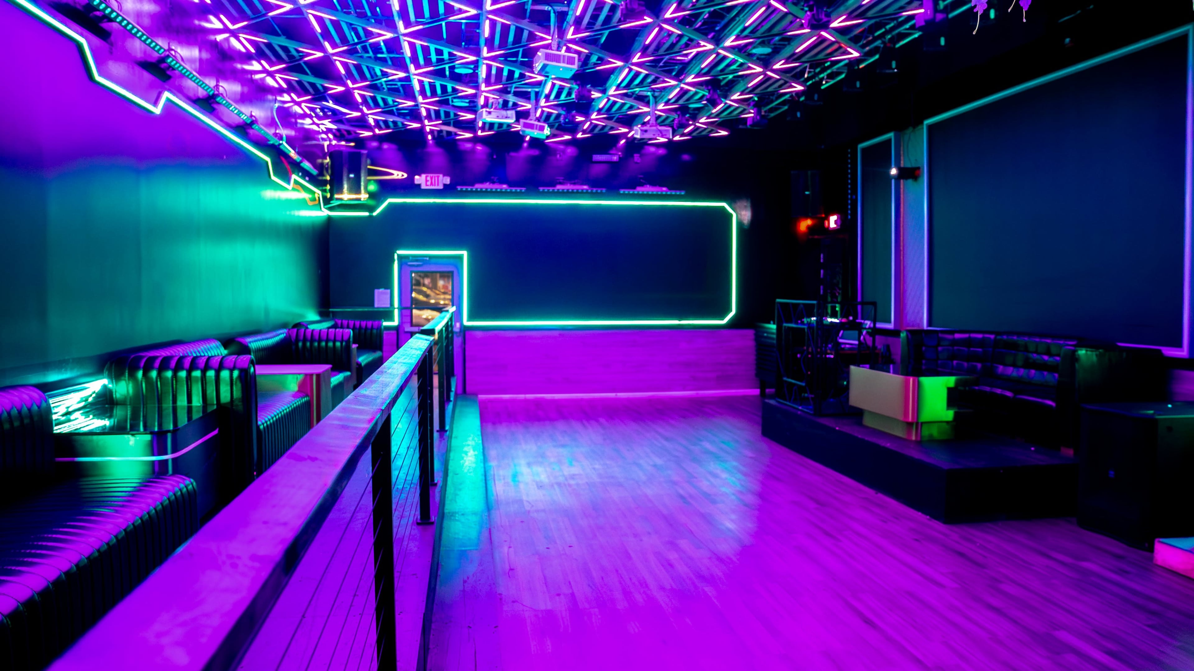 The image shows a vibrant nightclub interior with purple and blue LED lighting, a sleek bar area, and a spacious dance floor.