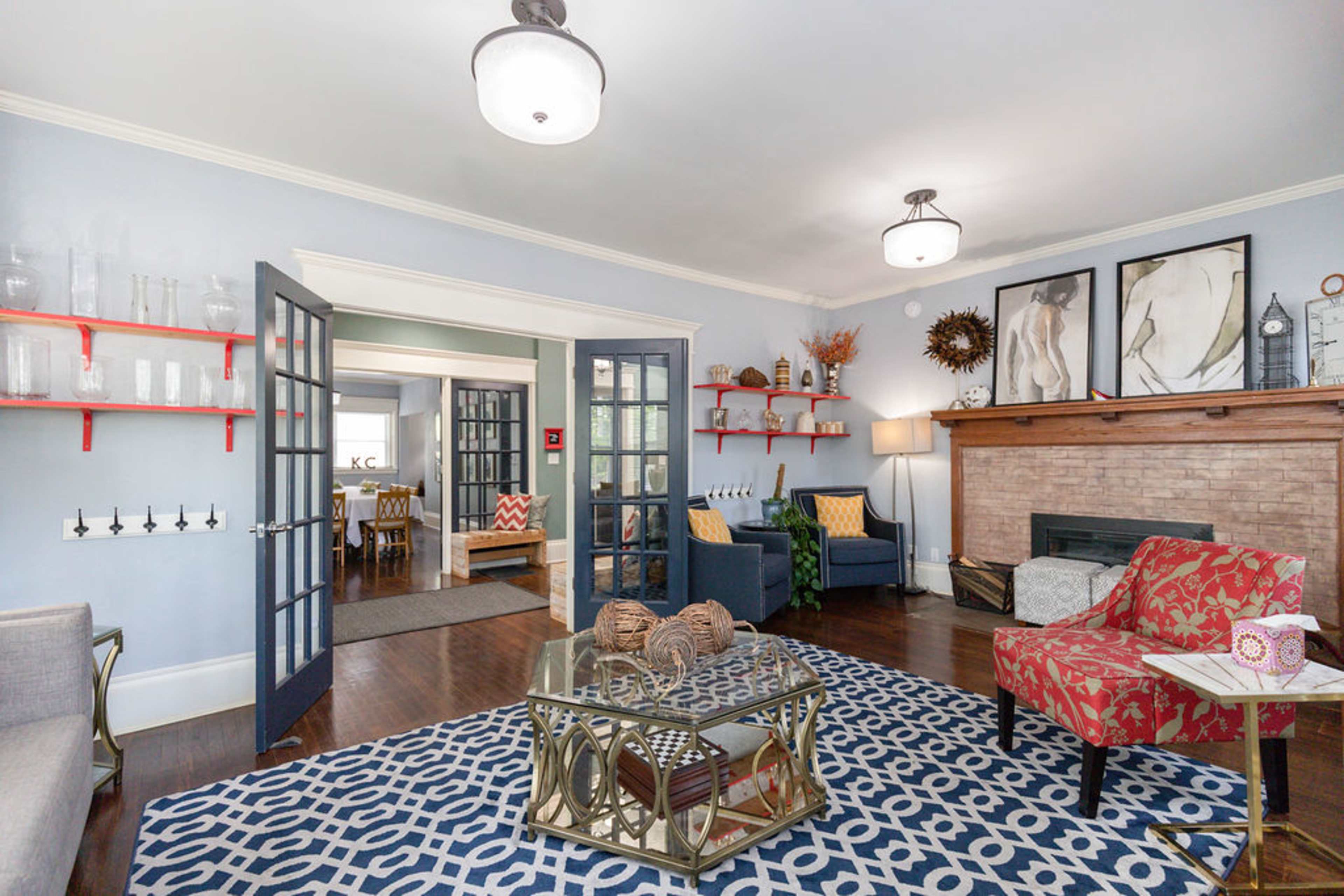 The living room features a fireplace, symmetrical seating arrangements, and decorative shelving against light blue walls.