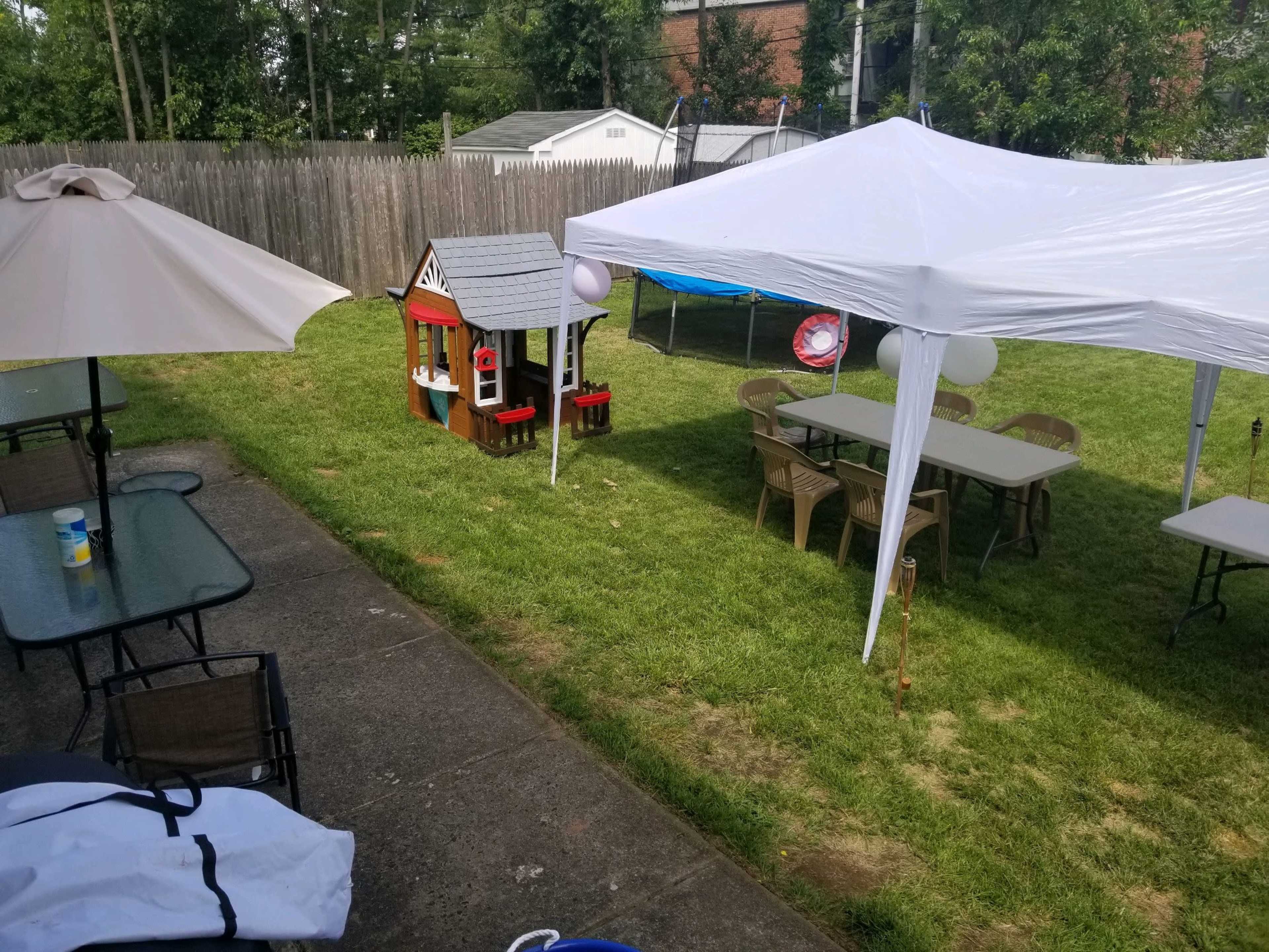 A backyard with a grassy area containing a playhouse, several tables under white canopies, and patio furniture.