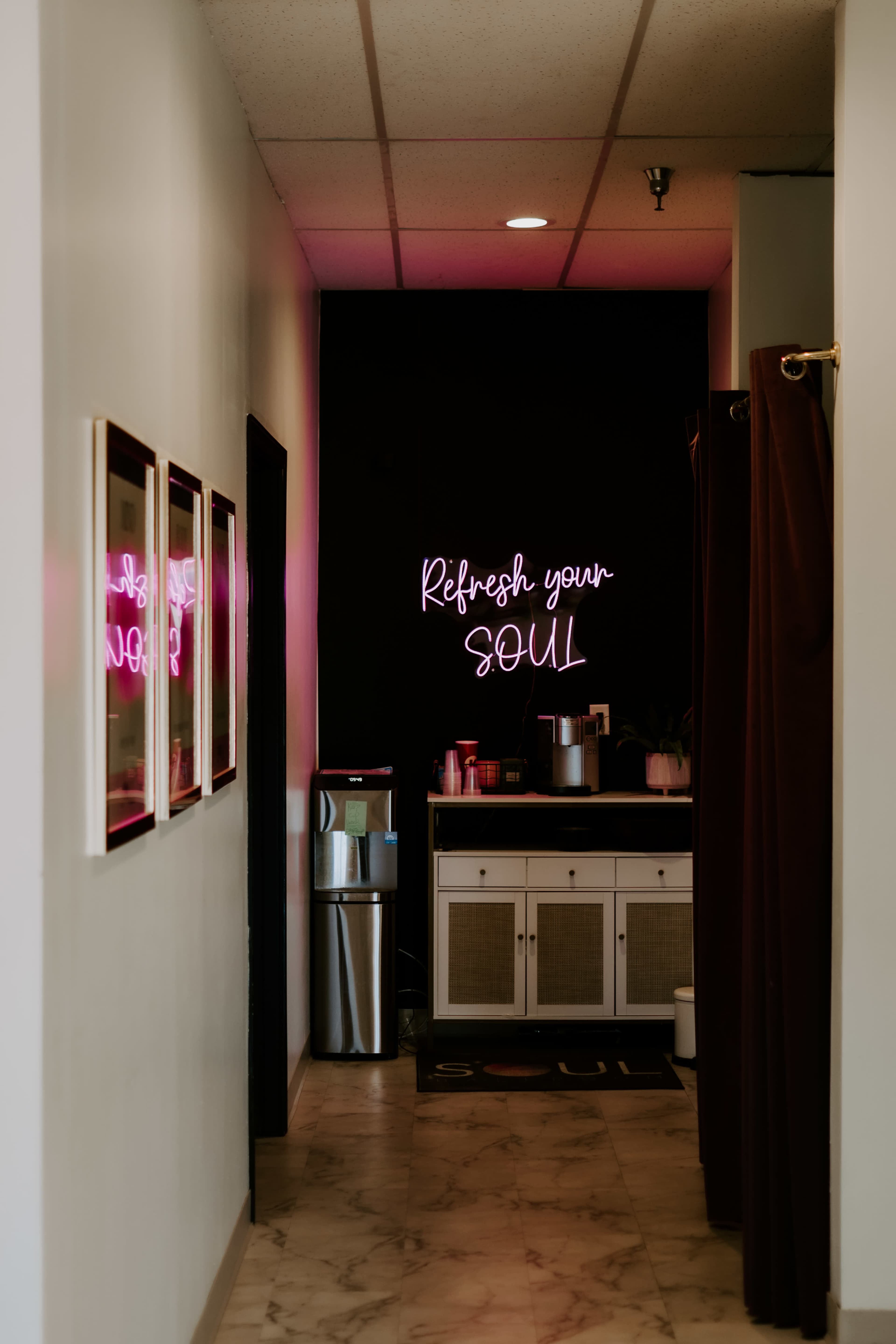 A narrow hallway features a wall with a neon sign that reads "Refresh your SOUL" and a small kitchenette area with a refrigerator and a countertop.
