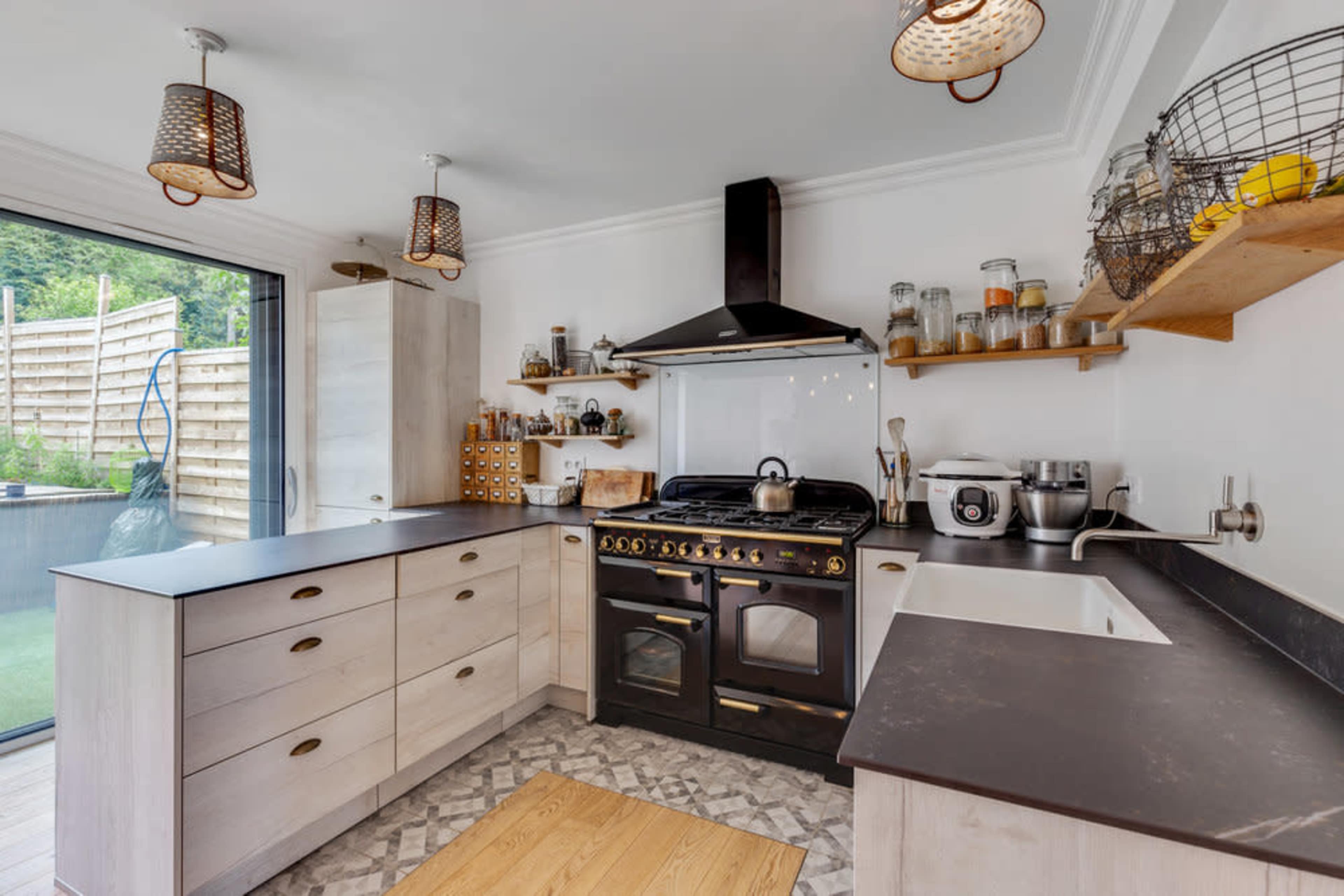 A modern kitchen featuring a black and silver oven, wooden cabinets, a stone countertop, and a glass sliding door leading to an outdoor area.
