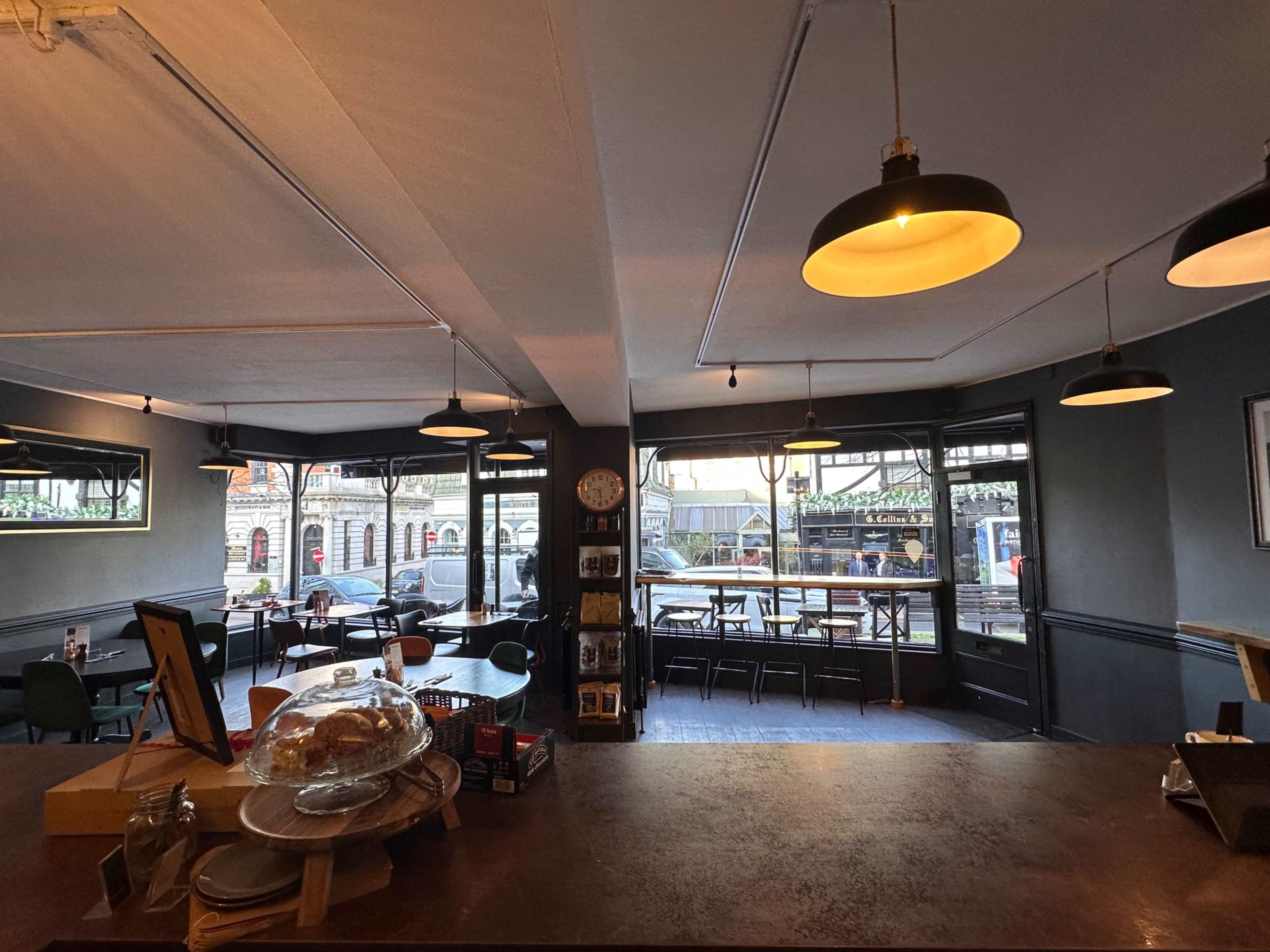 The image shows the interior of a café with tables, chairs, and large windows displaying a view of the street outside.