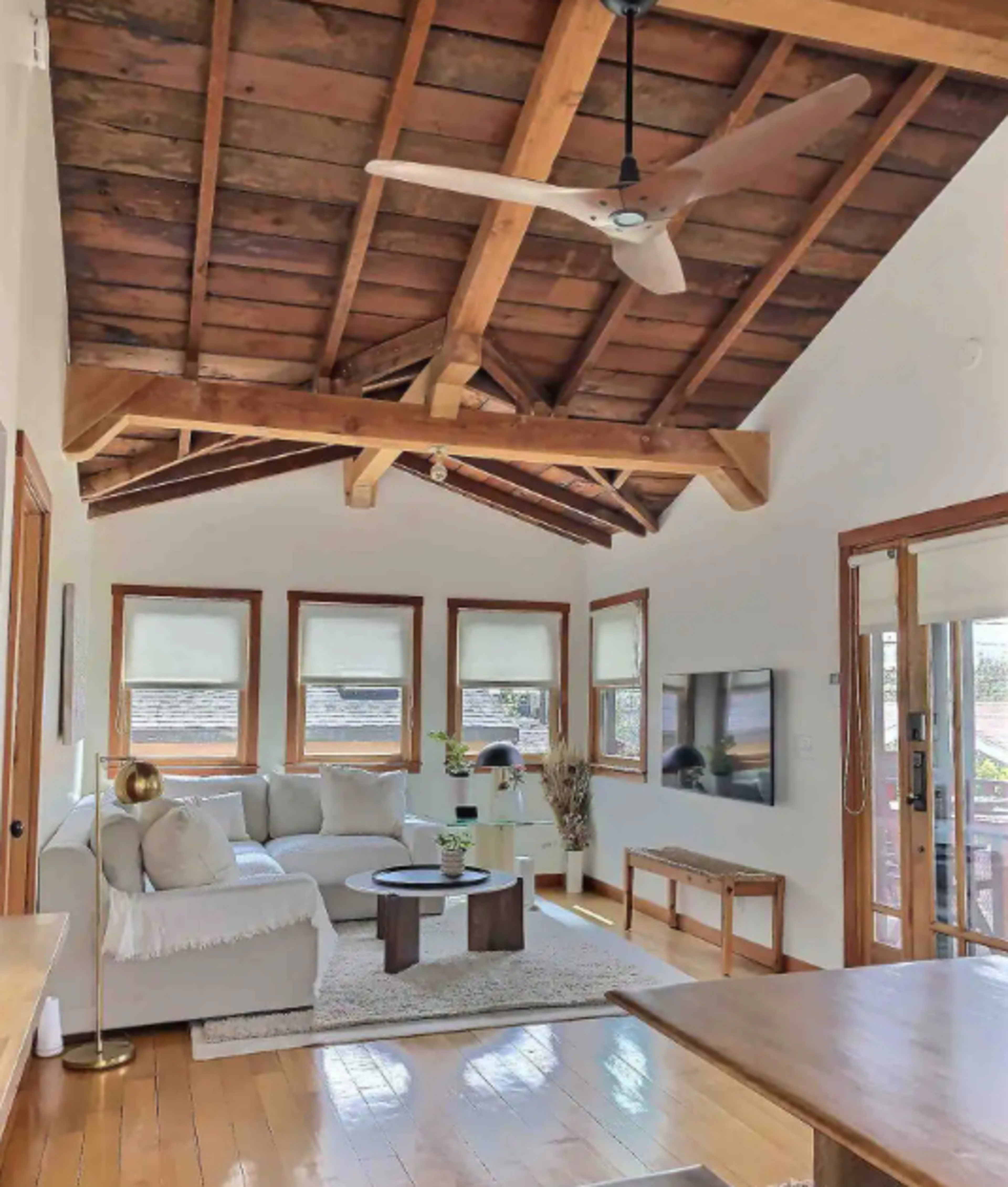 A living room with a high wooden ceiling, a beige sectional sofa, a round coffee table, and a large window letting in natural light.