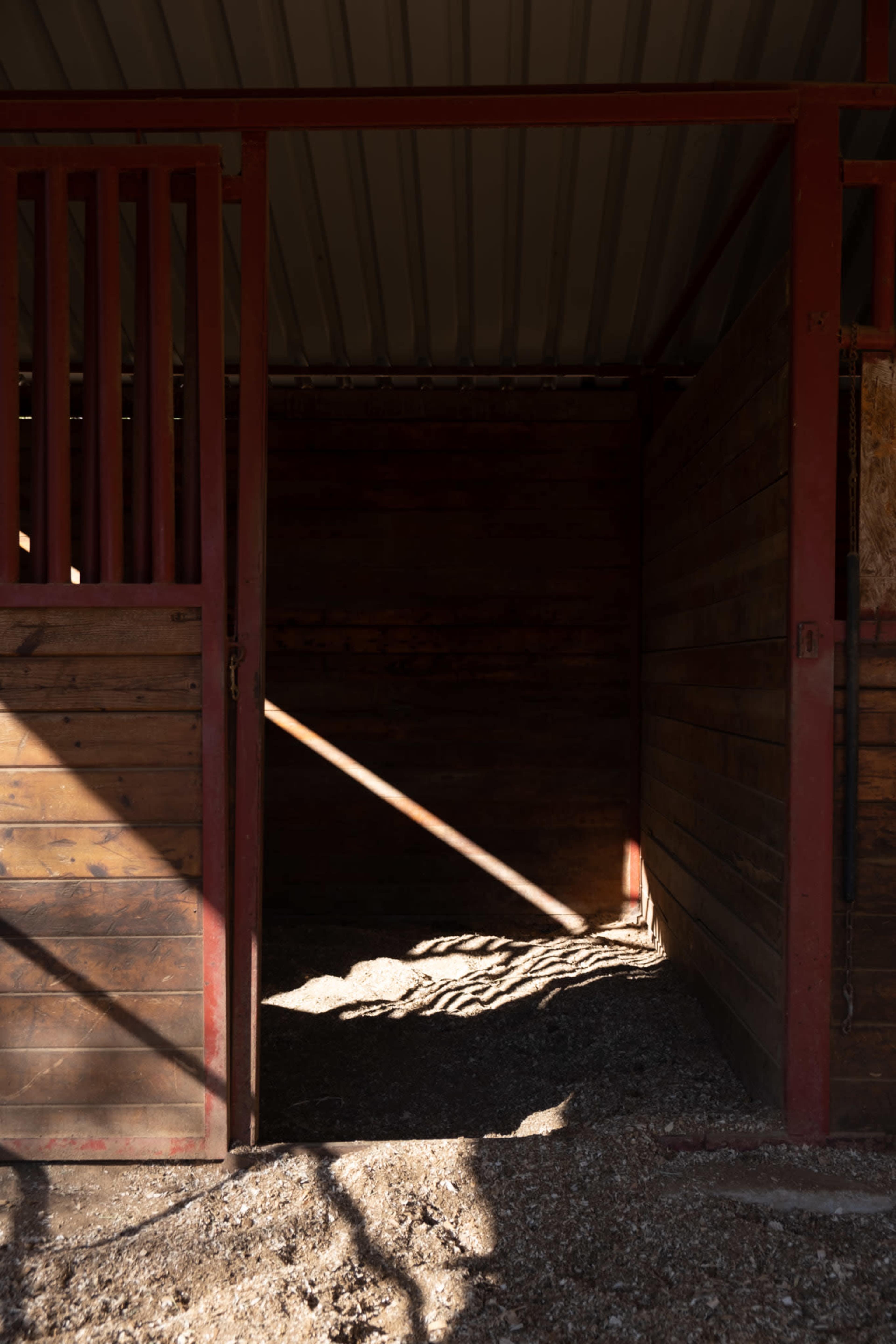 The interior of a barn features wooden walls and empty stalls, illuminated by a beam of sunlight.